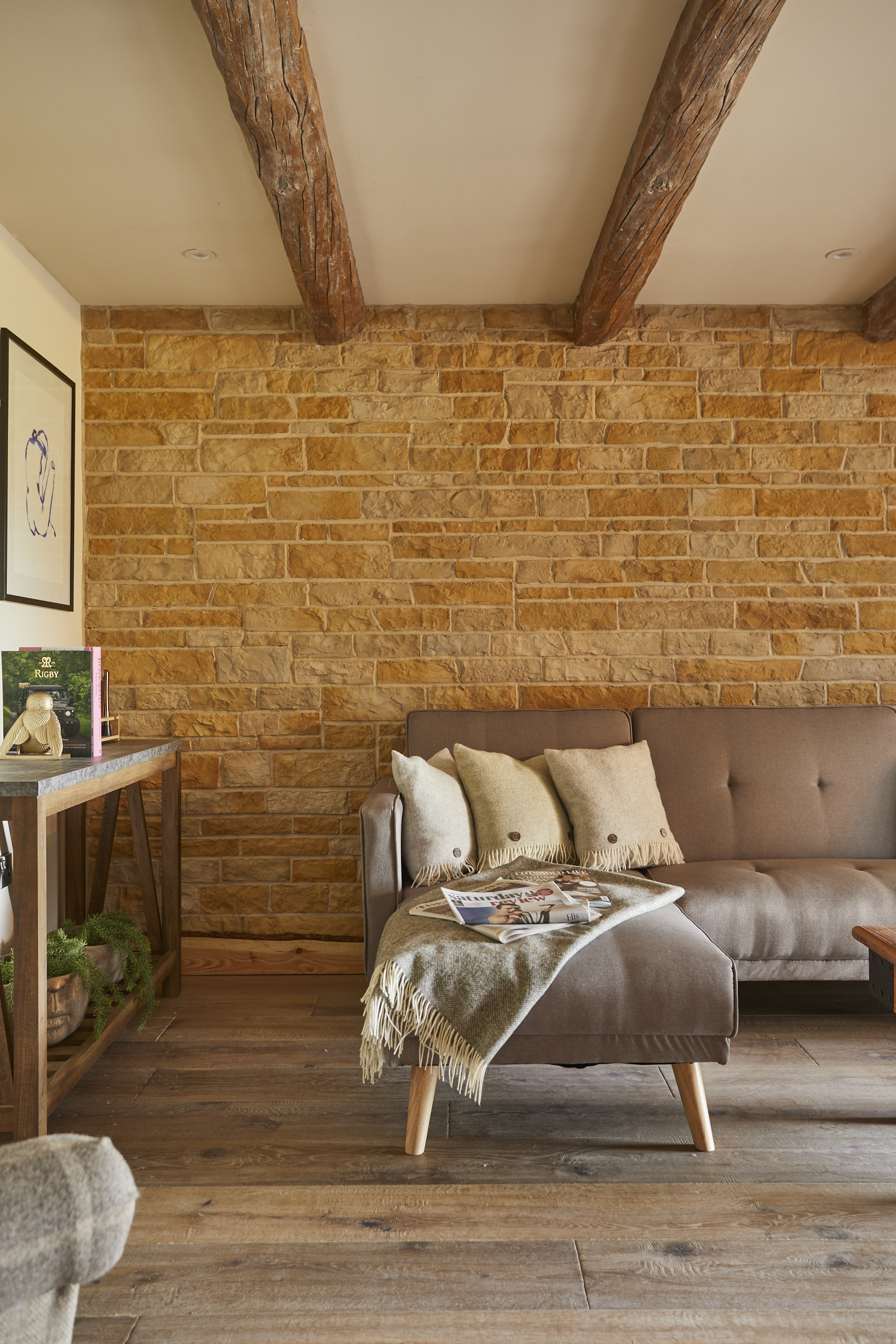 Cozy living room with wooden beams, stone accent wall, and tan sofa decorated with pillows and a throw blanket. - Wild Thyme & Honey Hotel in the Cotswolds