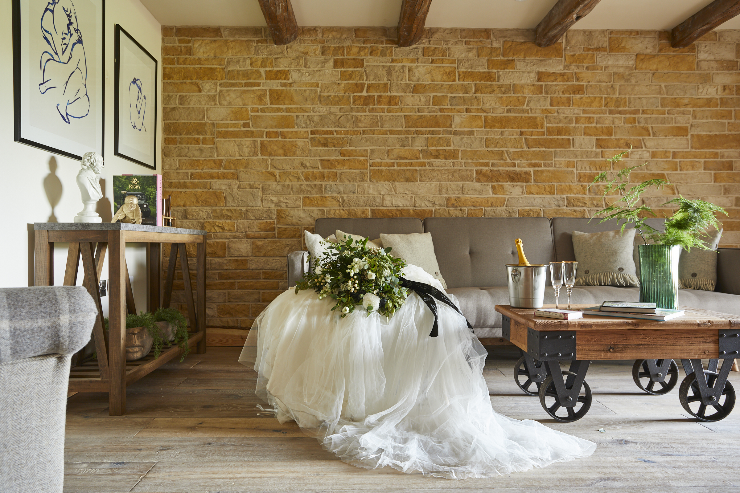 Wedding dress draped over a sofa in a rustic living room with stone wall, wooden beams, and a coffee table. - Wild Thyme & Honey Hotel in the Cotswolds