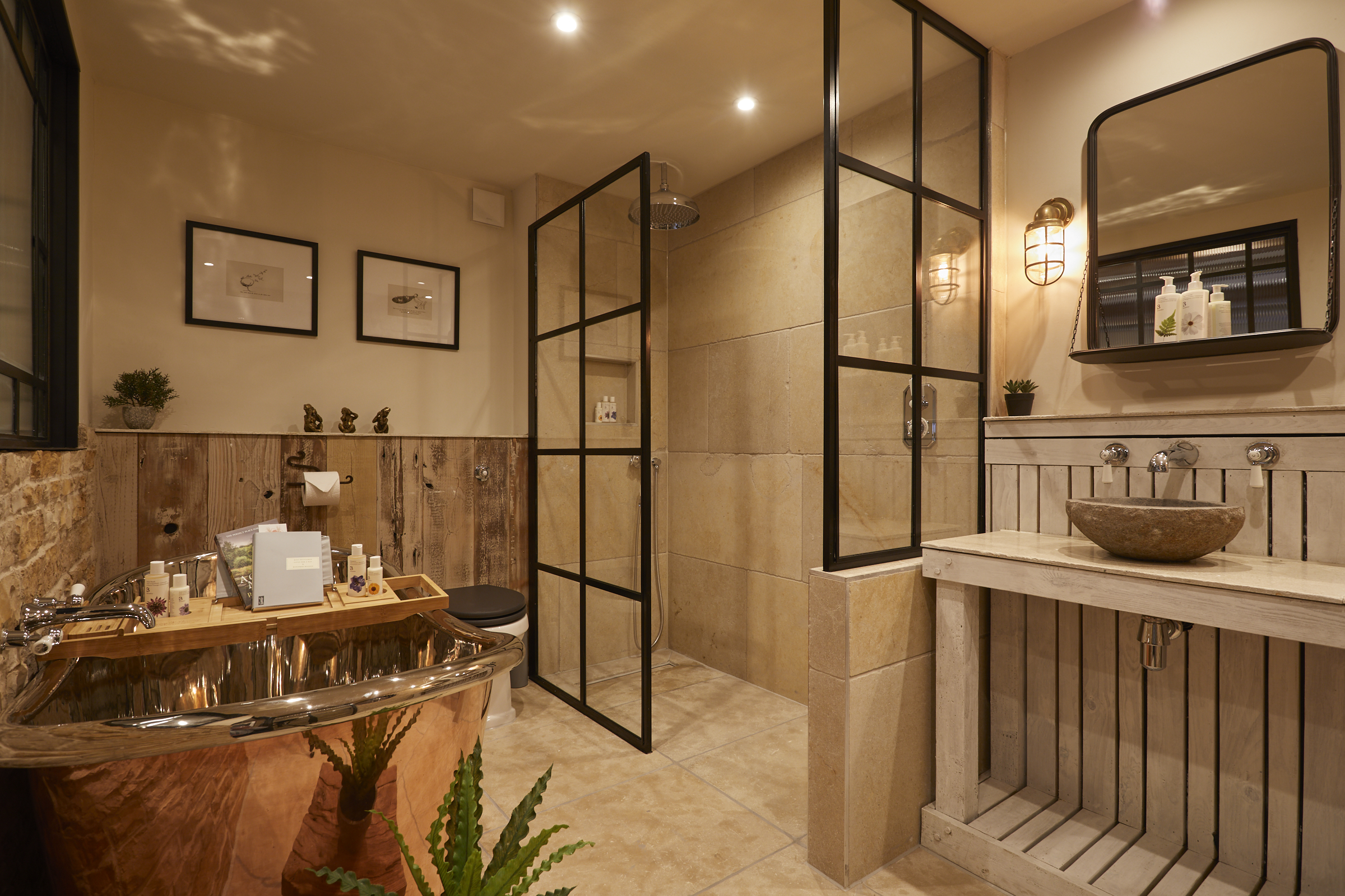 Luxurious bathroom with copper bathtub, wood and stone accents, modern glass shower, and stylish sink with lit mirror. - Wild Thyme & Honey Hotel in the Cotswolds