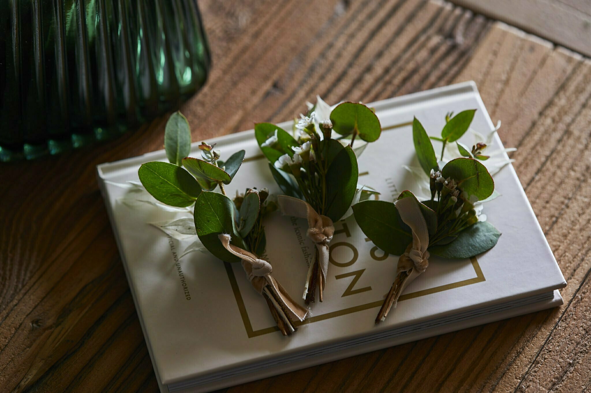Small bouquets of greenery with ribbons on a book on a wooden table next to a green glass vase. - Wild Thyme & Honey Hotel in the Cotswolds