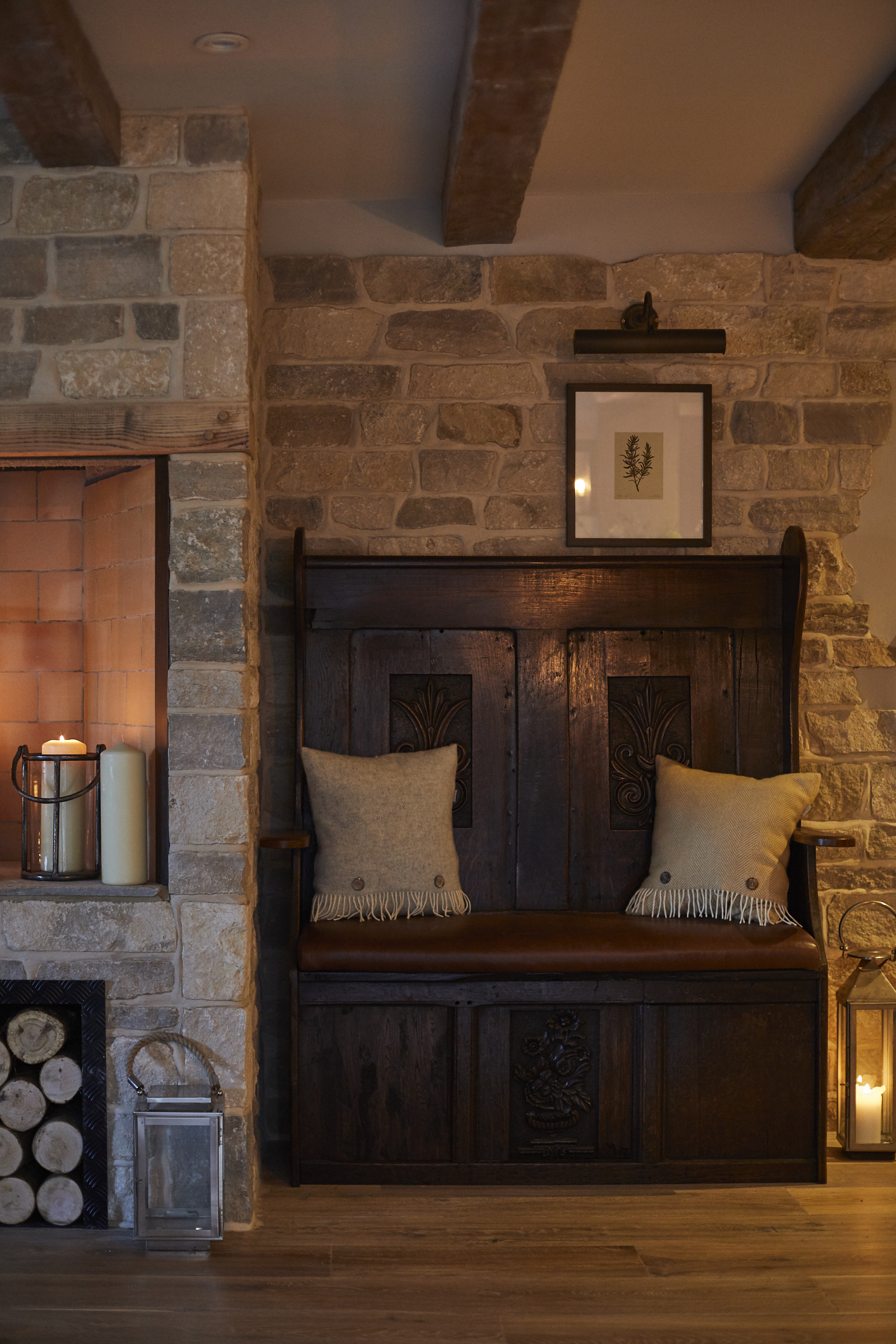 Rustic room with a wooden bench, stone walls, candles, and framed art. Warm lighting and cozy ambiance complete the scene. - Wild Thyme & Honey Hotel in the Cotswolds