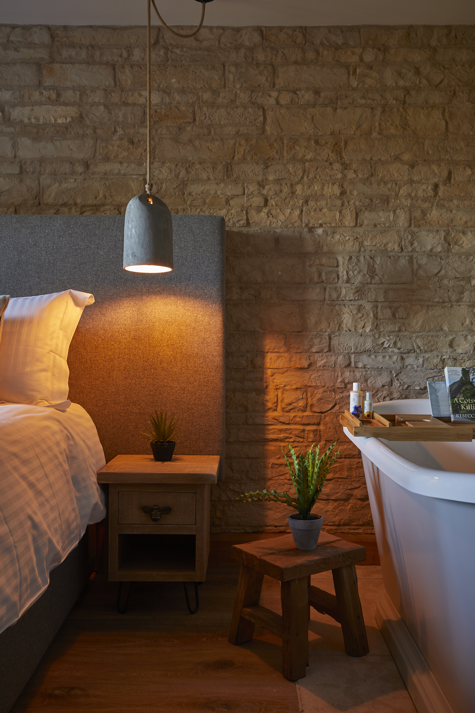 Cozy bedroom with exposed brick wall, bed, hanging light, wooden nightstand with plant, and a freestanding bathtub. - Wild Thyme & Honey Hotel in the Cotswolds