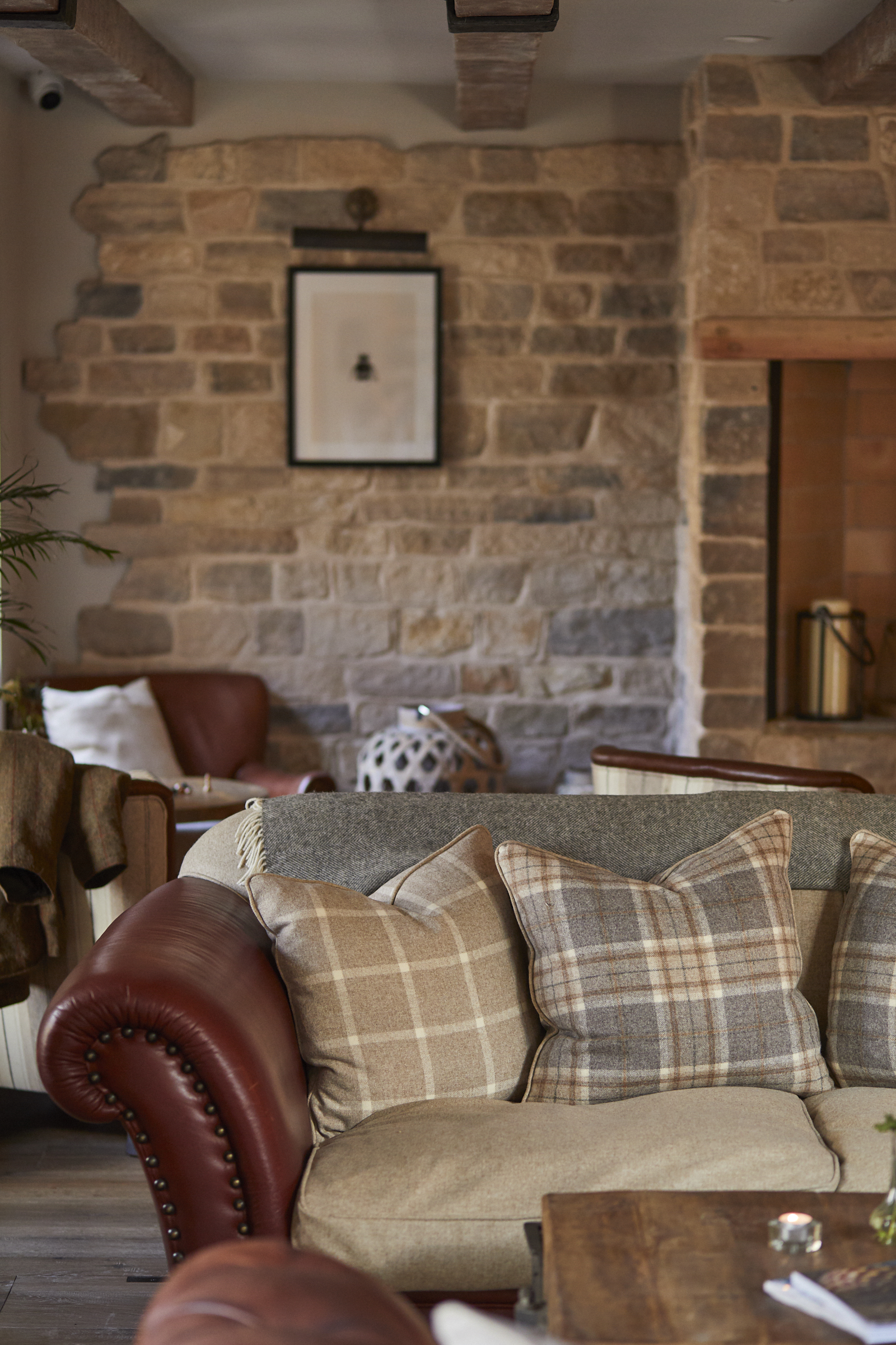 Cozy living room with stone walls, a leather sofa with plaid cushions, and rustic wooden beams and furnishings. - Wild Thyme & Honey Hotel in the Cotswolds