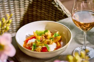 A bowl of fresh peach slices, tomatoes, cheese, and basil leaves on a table next to a glass of rosé wine. - Wild Thyme & Honey Hotel in the Cotswolds