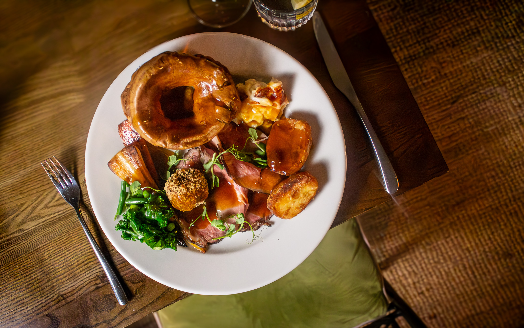 Plate of roast beef, Yorkshire pudding, and greens with sides and red wine on a wooden table. - Wild Thyme & Honey Hotel in the Cotswolds