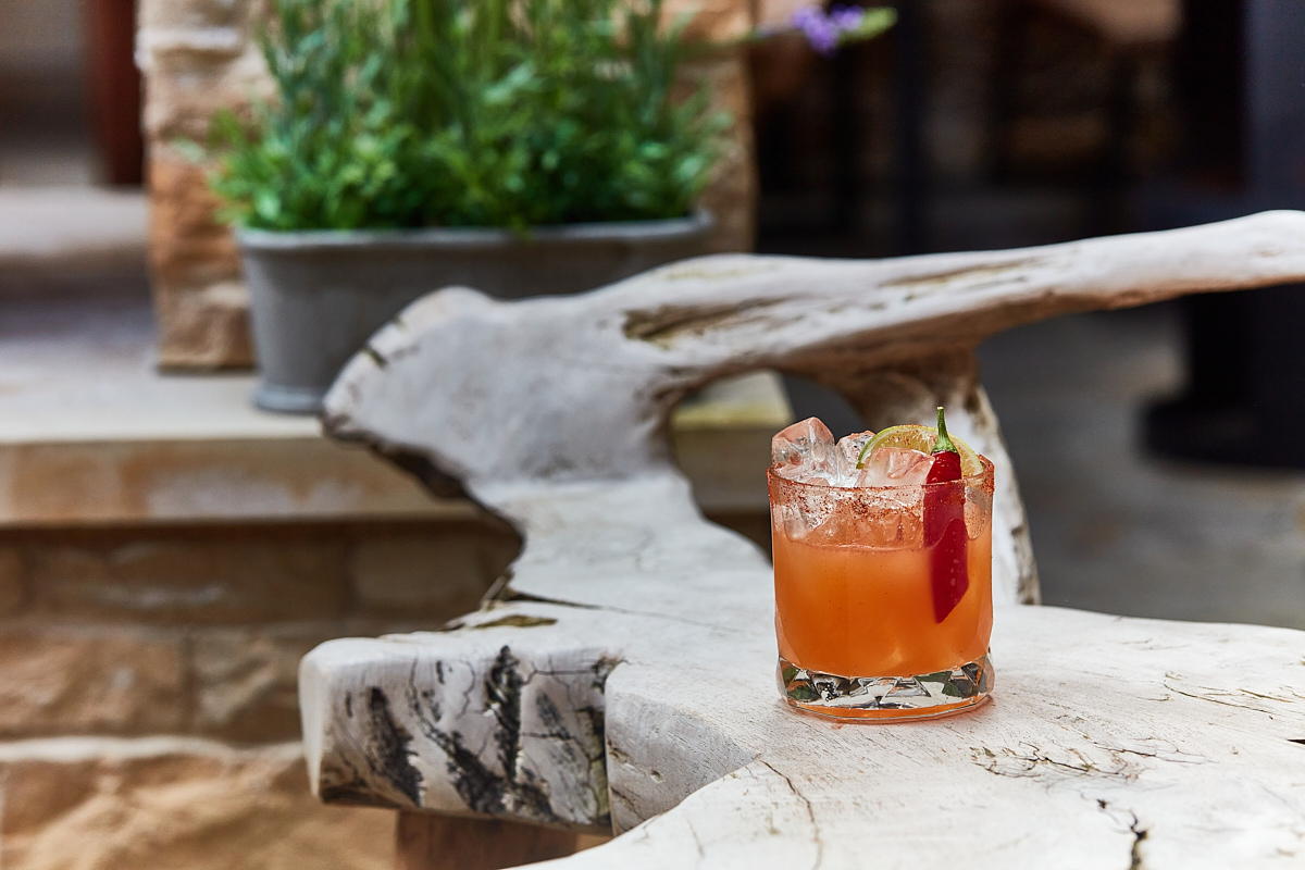 A glass of iced cocktail with citrus garnish on a rustic, marble-like bench in an outdoor setting. - Wild Thyme & Honey Hotel in the Cotswolds