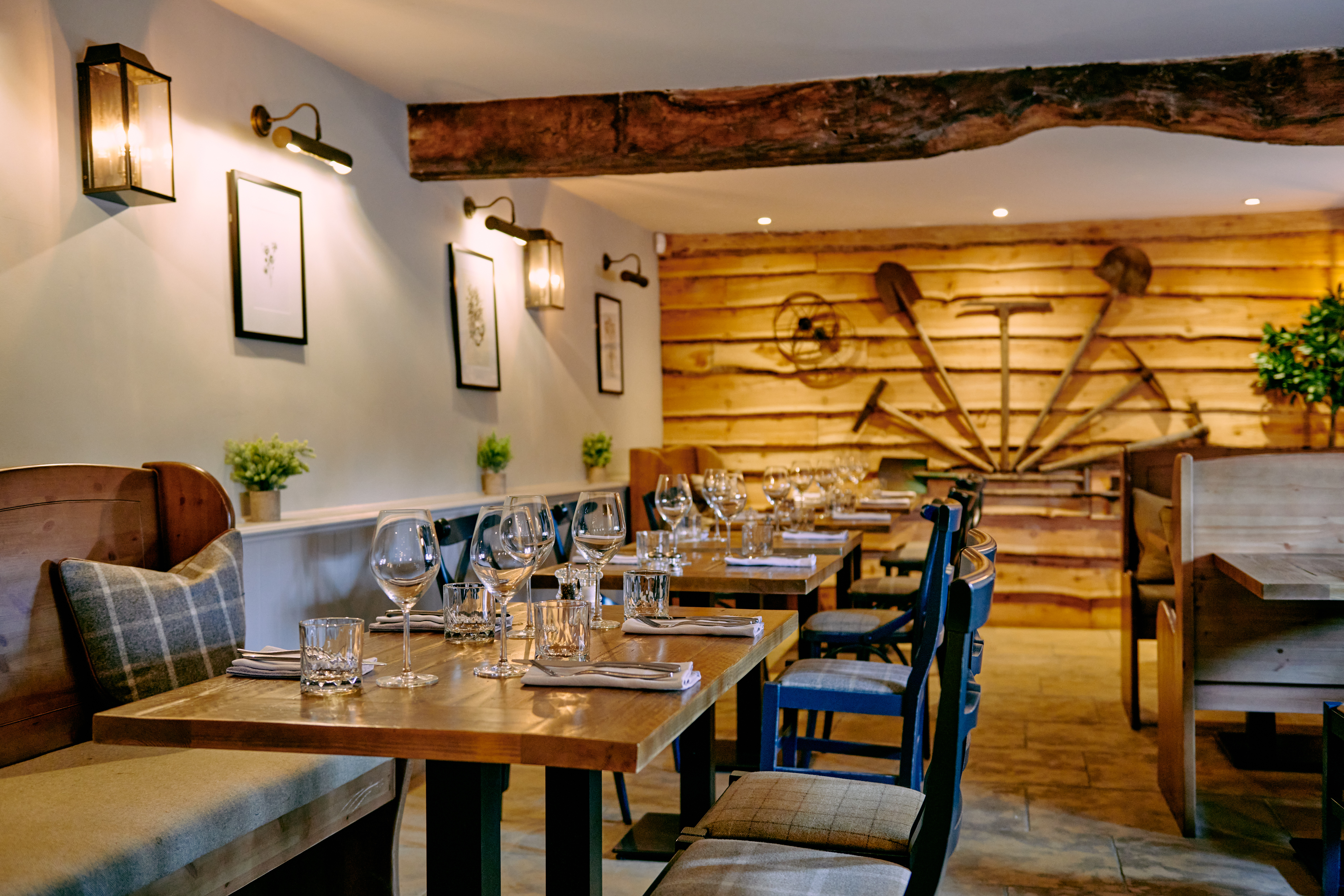 Cozy restaurant interior with wooden tables set for dining, rustic wall decor of tools, and soft lighting creating a warm ambiance. - Wild Thyme & Honey Hotel in the Cotswolds