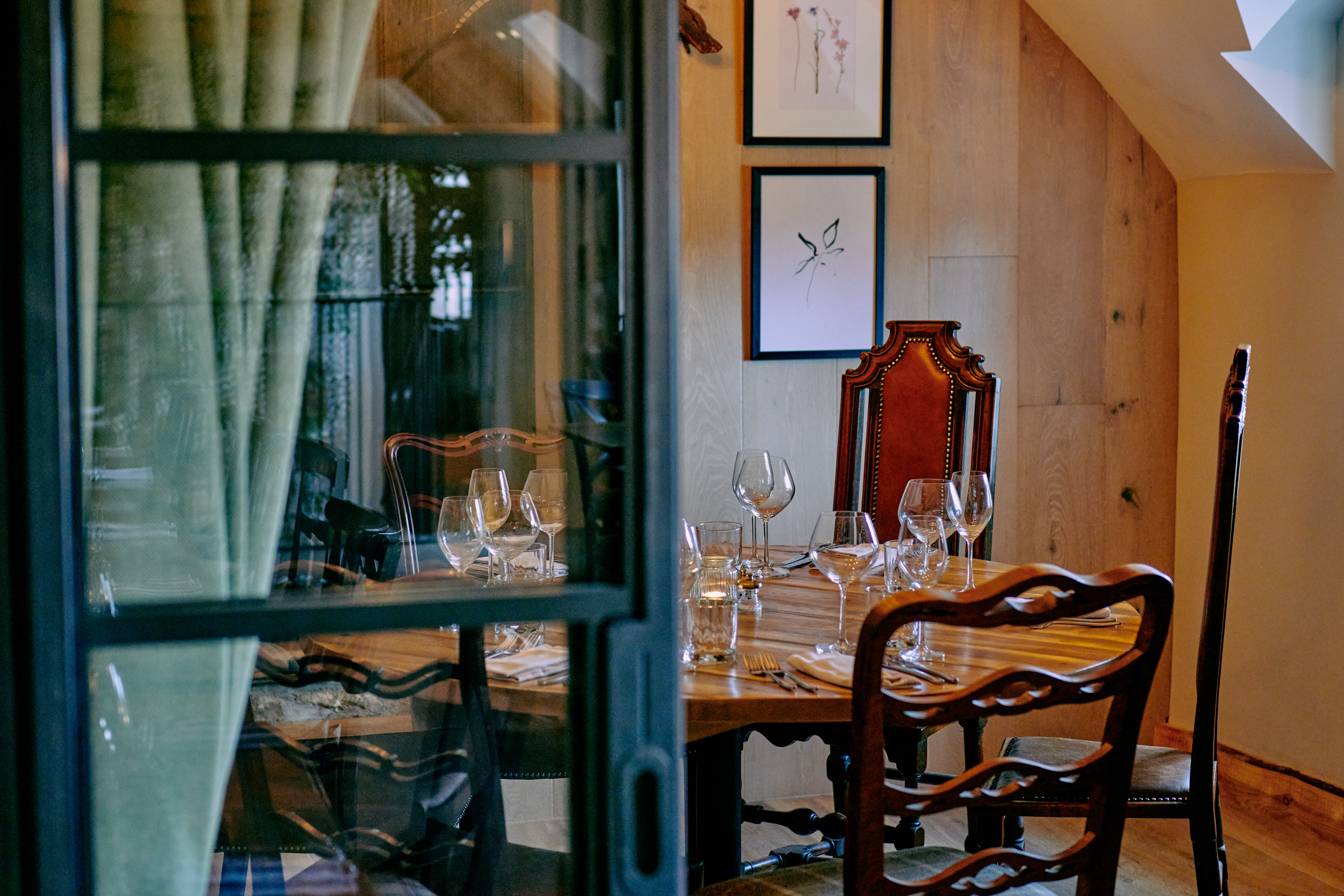 A cozy dining room with a wooden table set for four, featuring elegant chairs, glassware, and framed art on the wall. - Wild Thyme & Honey Hotel in the Cotswolds