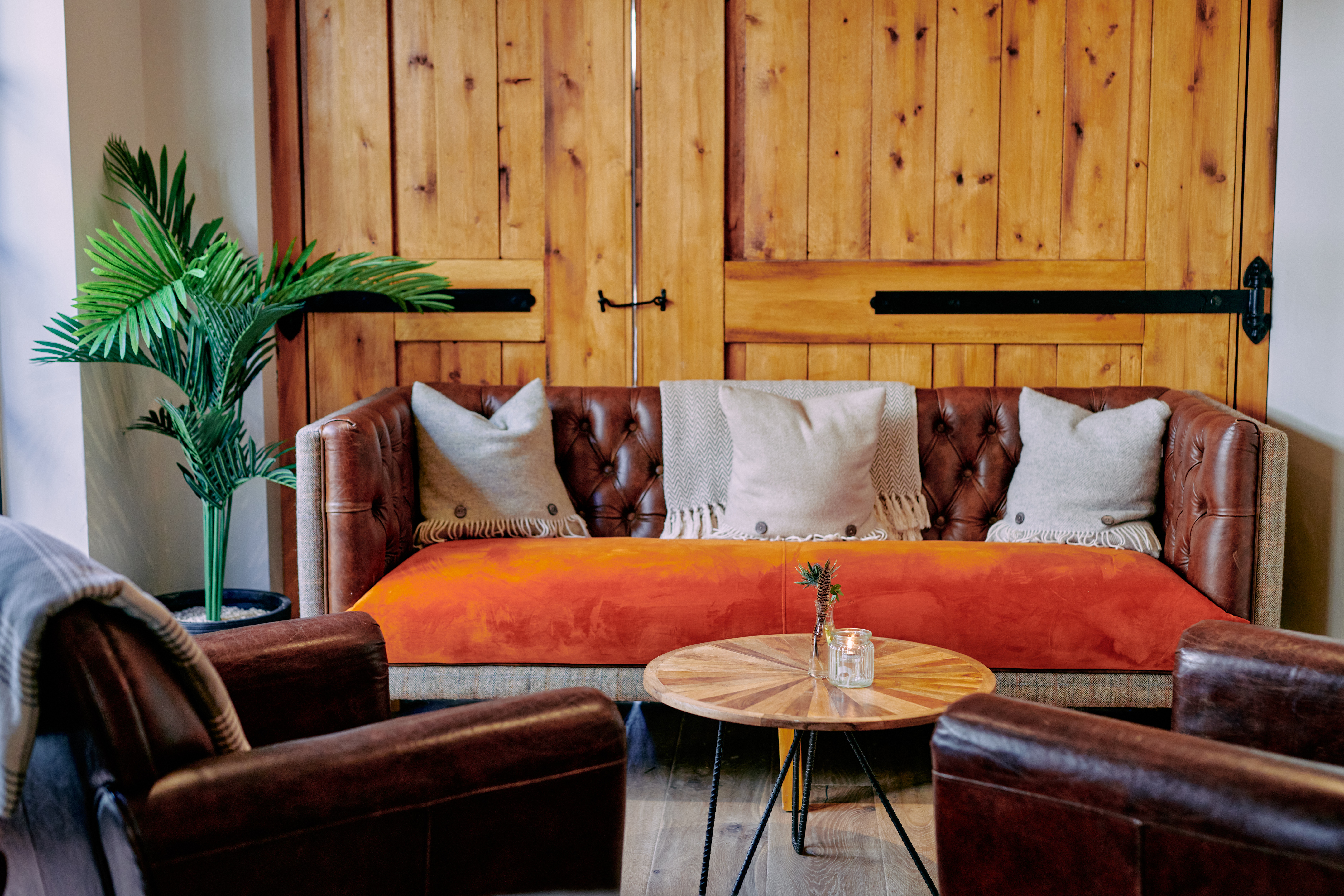 Cozy room with a brown leather sofa adorned with pillows and a throw, a wooden coffee table, and a potted plant nearby. - Wild Thyme & Honey Hotel in the Cotswolds