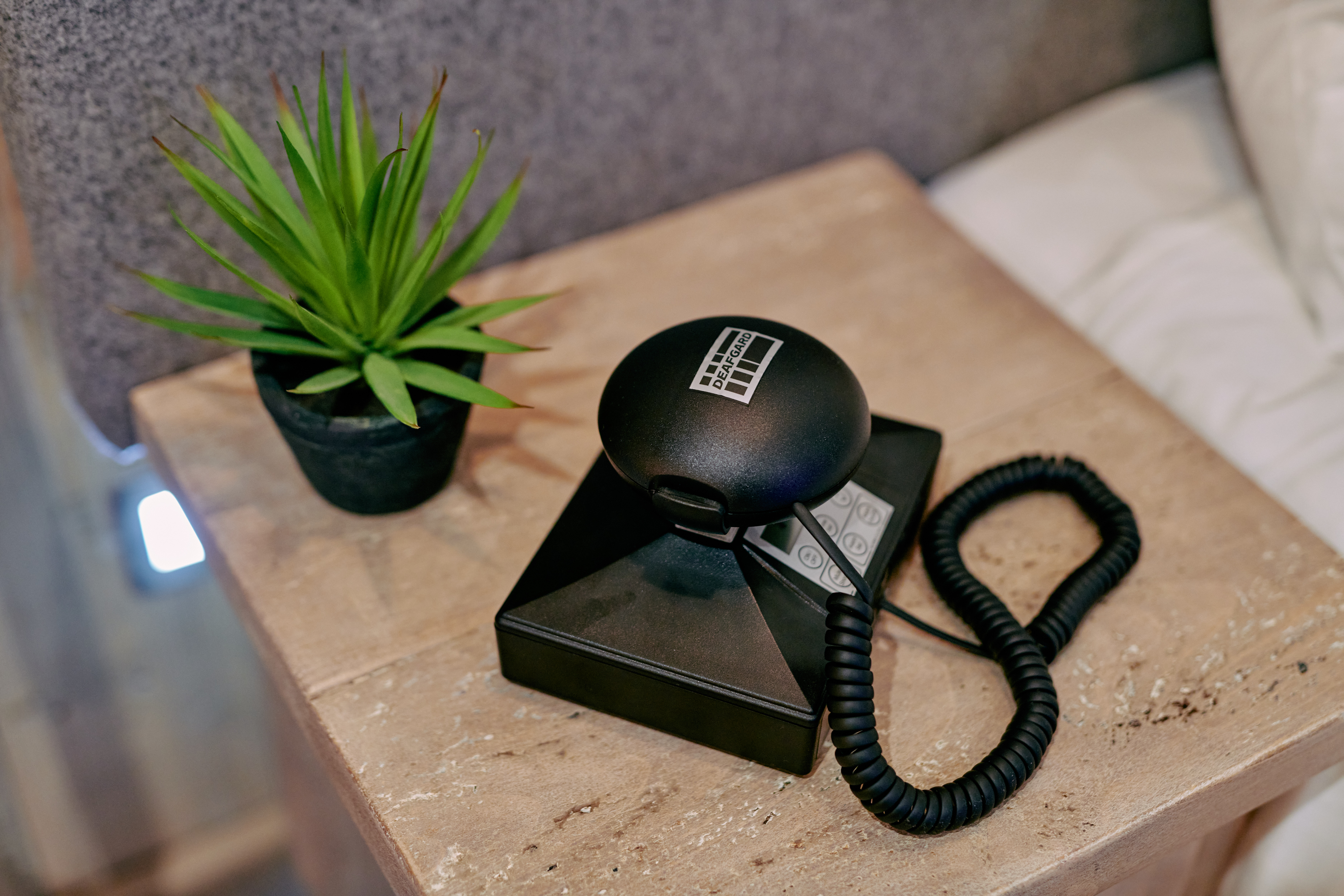 A black spherical device with a coiled cord on a wooden table beside a potted green plant. - Wild Thyme & Honey Hotel in the Cotswolds