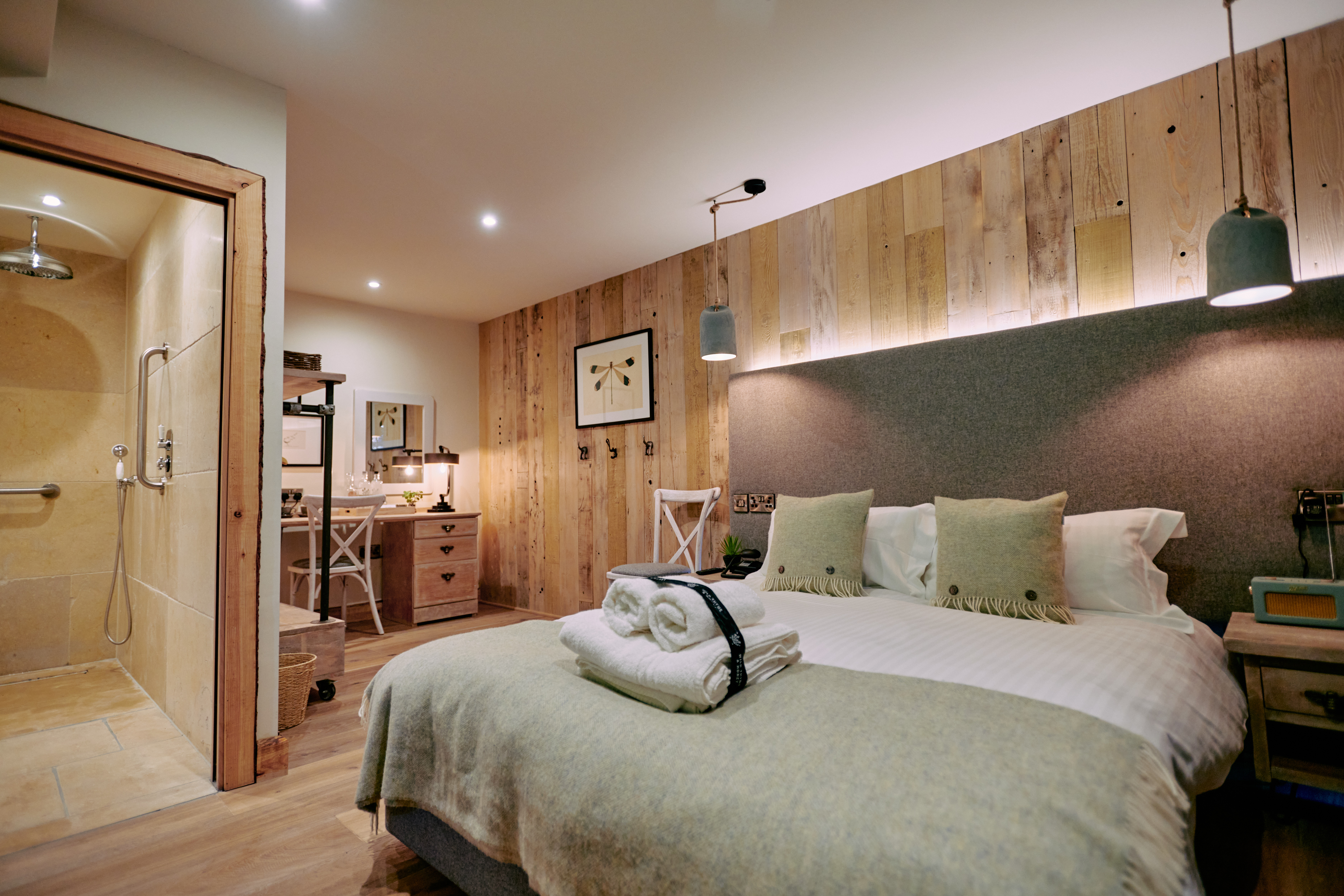 Cozy bedroom with a double bed, folded towels, a bathroom entrance, a desk, and soft lighting against wooden accents. - Wild Thyme & Honey Hotel in the Cotswolds