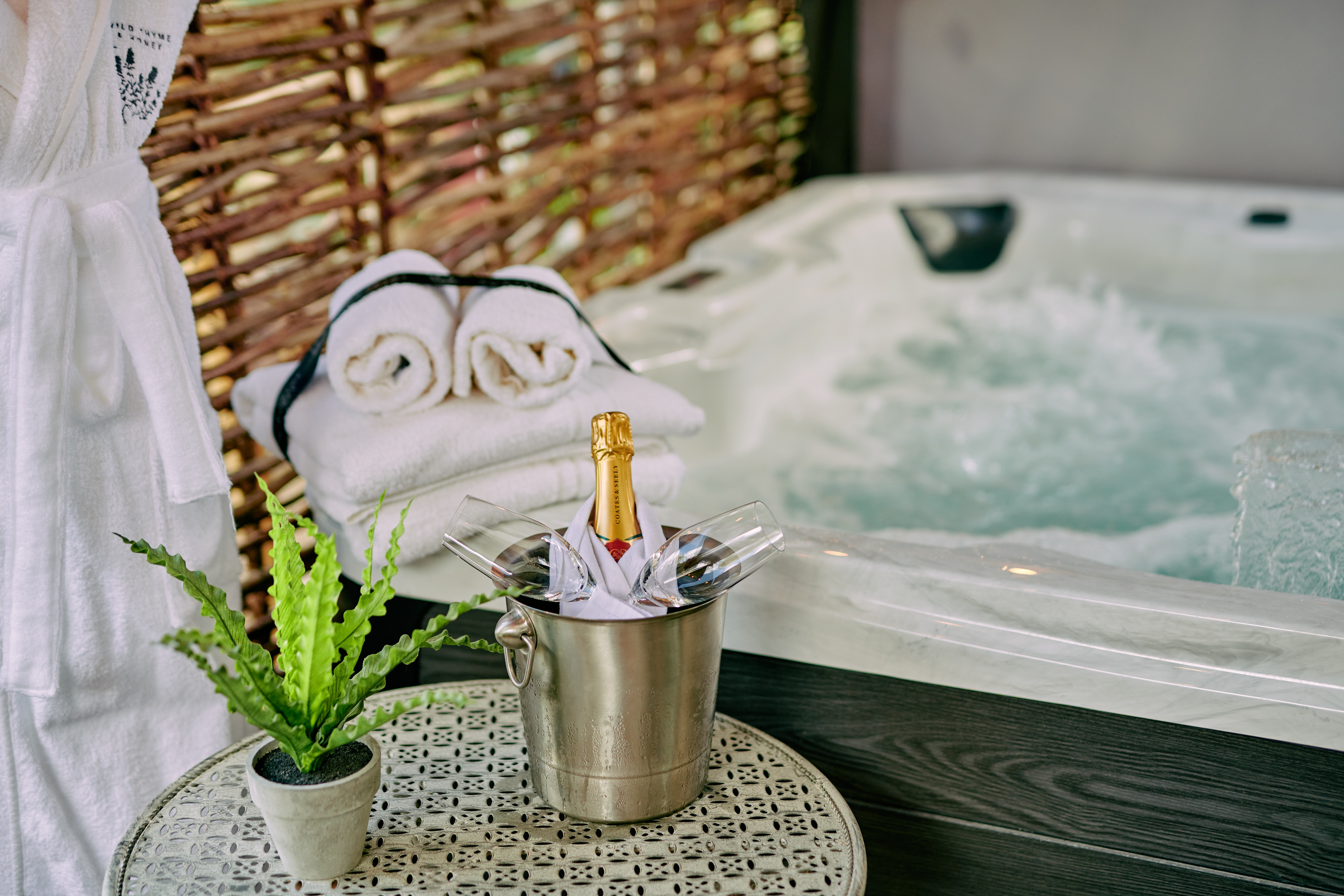 Luxurious hot tub with champagne in an ice bucket, two glasses, folded towels, and a plant on a side table. - Wild Thyme & Honey Hotel in the Cotswolds