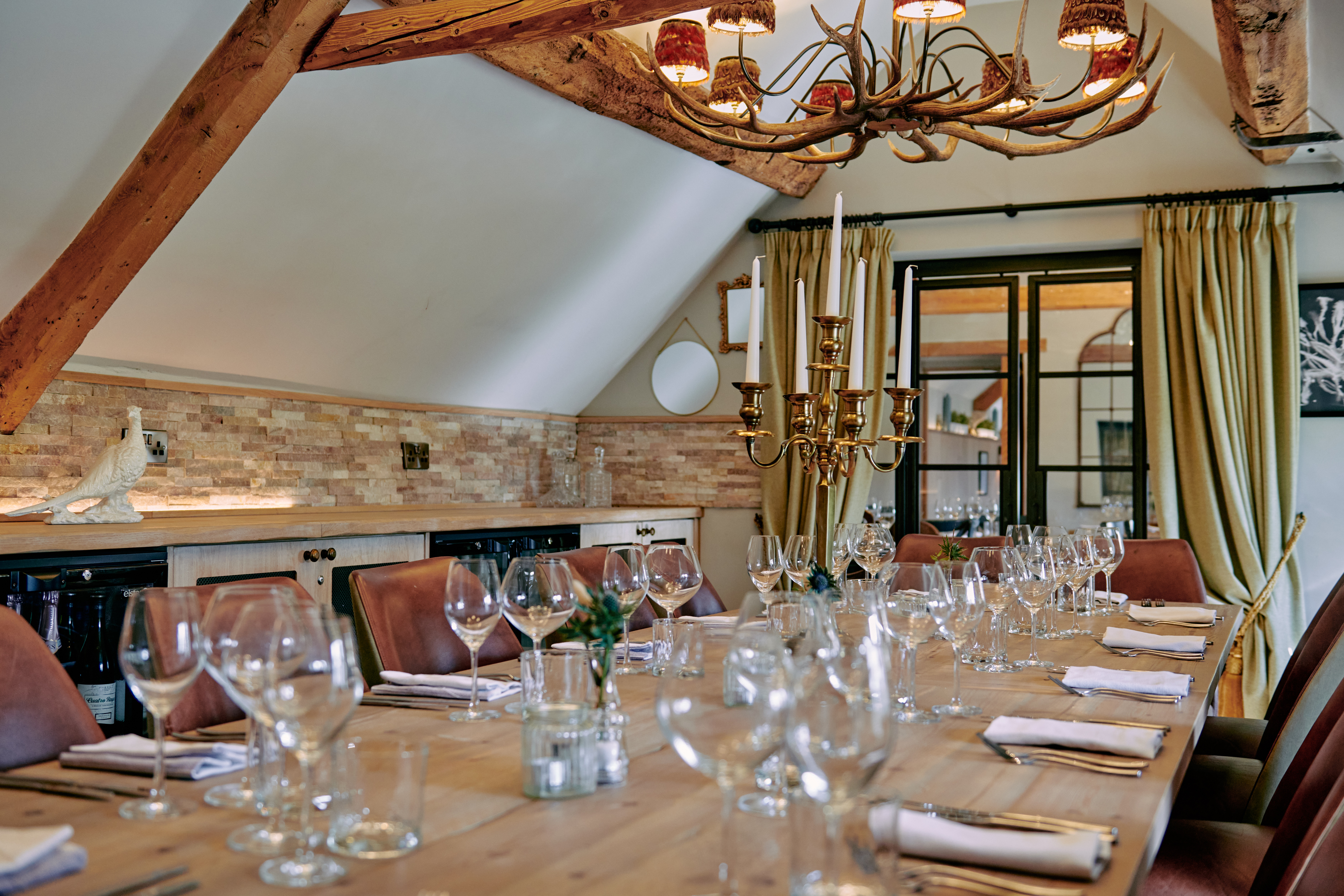 Elegant dining room with wooden table set for a meal, featuring wine glasses, brown chairs, a chandelier, and warm lighting. - Wild Thyme & Honey Hotel in the Cotswolds