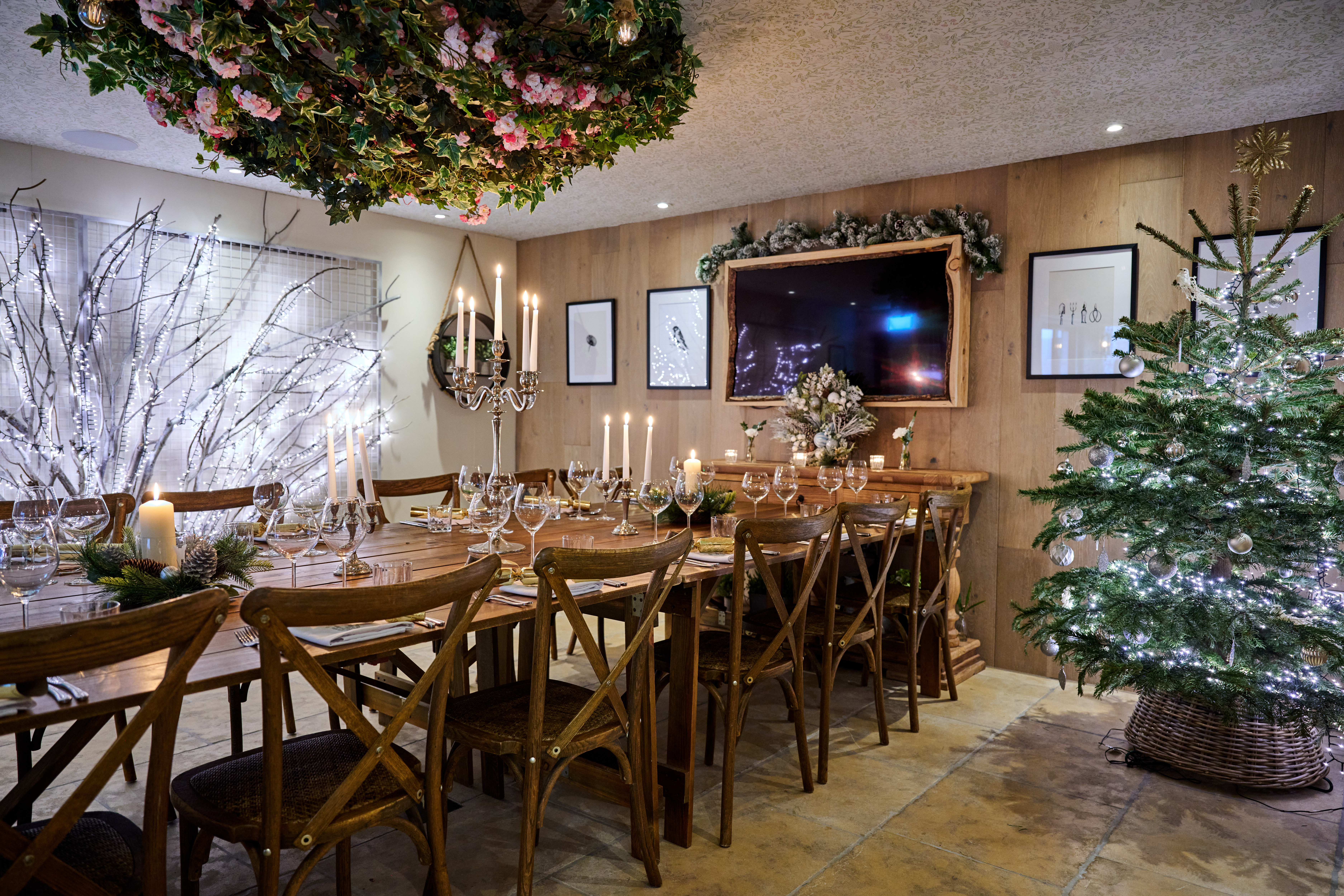 Elegant dining room with a long wooden table set with candles and glassware. A decorated Christmas tree stands nearby. - Wild Thyme & Honey Hotel in the Cotswolds