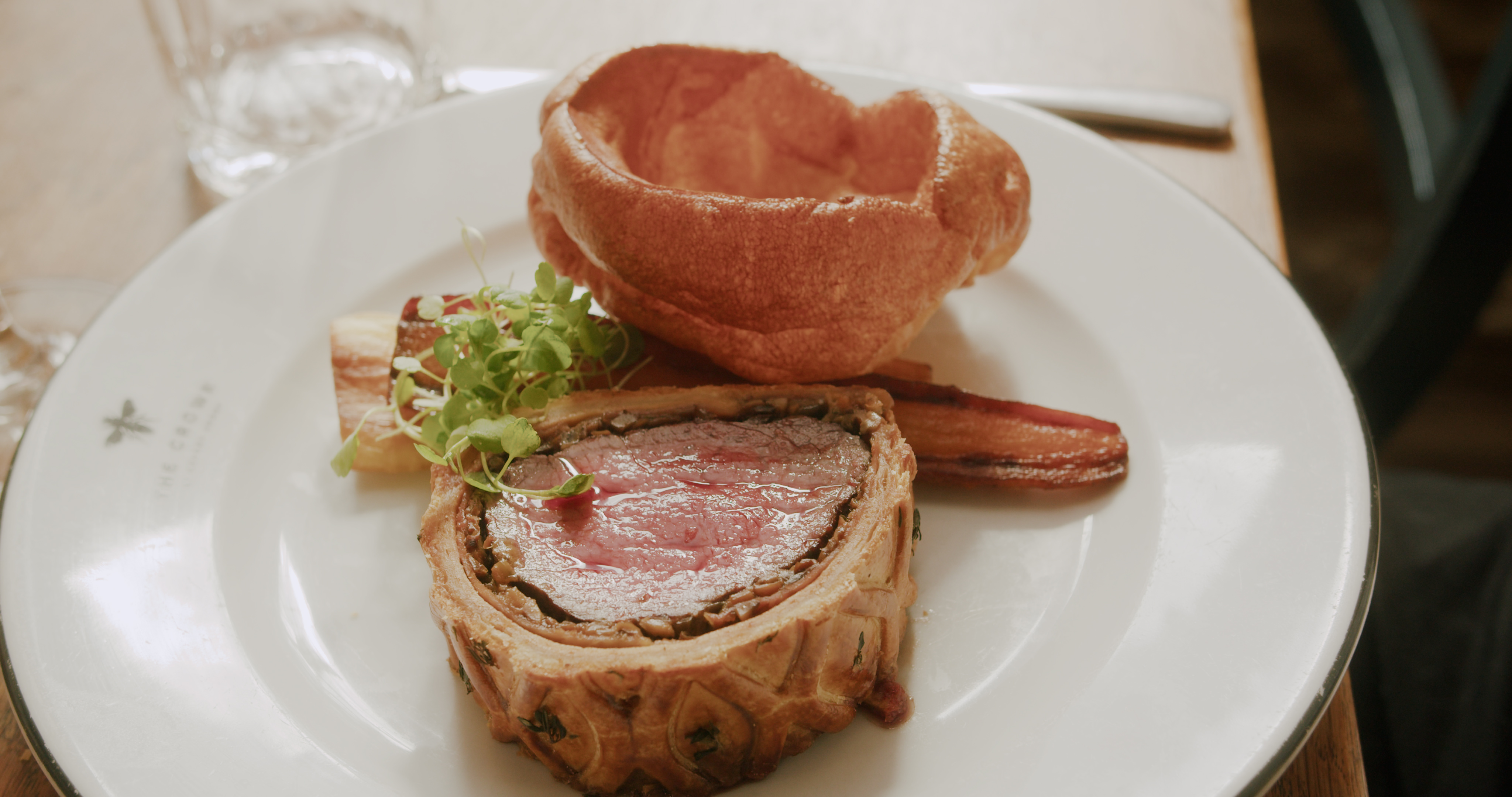 Beef Wellington slice with a Yorkshire pudding and a garnish, served on a white plate. - Wild Thyme & Honey Hotel in the Cotswolds