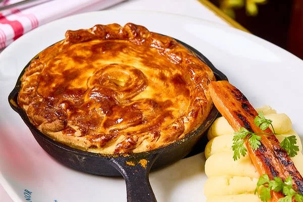 Golden pie in a skillet on a plate with mashed potatoes, roasted carrot, and garnish. - Wild Thyme & Honey Hotel in the Cotswolds