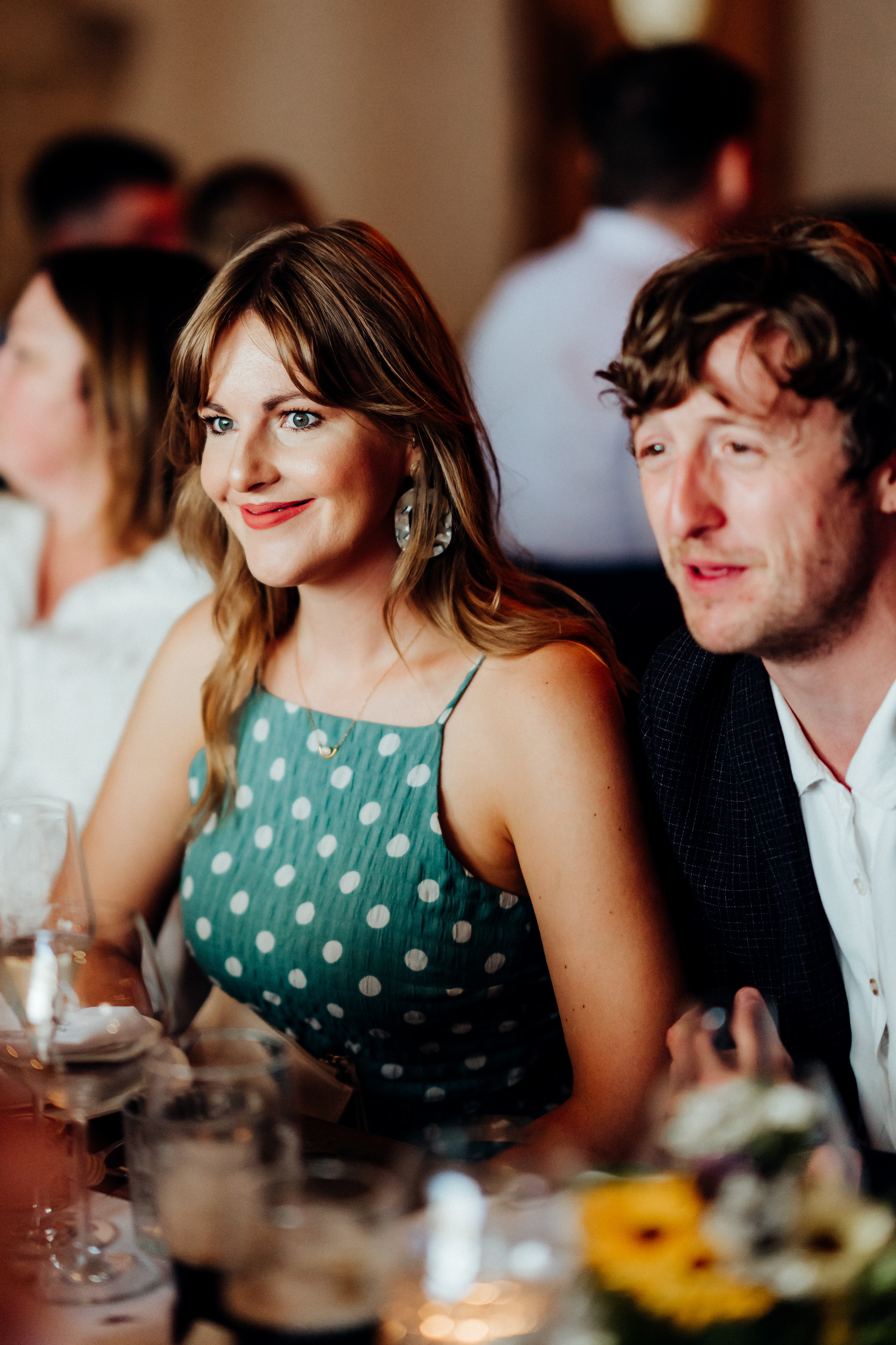 A woman in a green polka dot dress and a man sit together at a table, smiling and chatting at a social event. - Wild Thyme & Honey Hotel in the Cotswolds