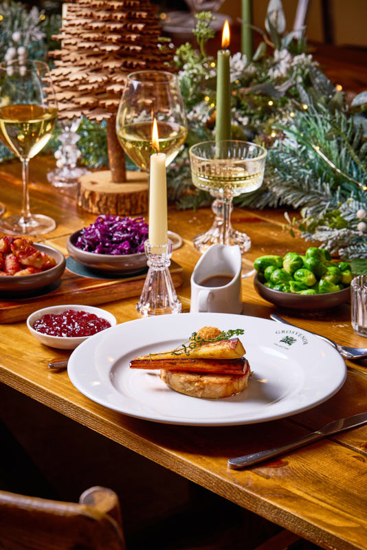 Festive dinner table with wine, candles, roast dish, Brussels sprouts, red cabbage, and cranberry sauce. Holiday decorations present. - Wild Thyme & Honey Hotel in the Cotswolds