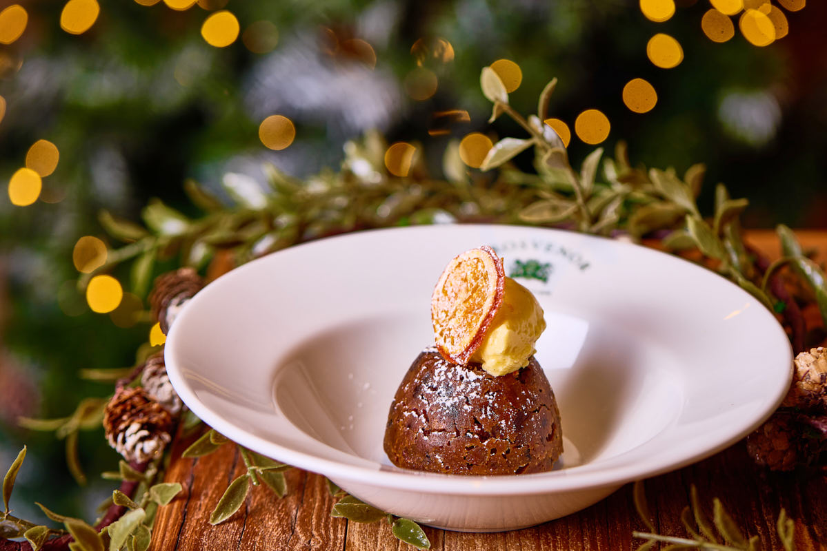 Festive dessert plated with a scoop of ice cream and a candied orange slice, surrounded by holiday decorations and lights. - Wild Thyme & Honey Hotel in the Cotswolds