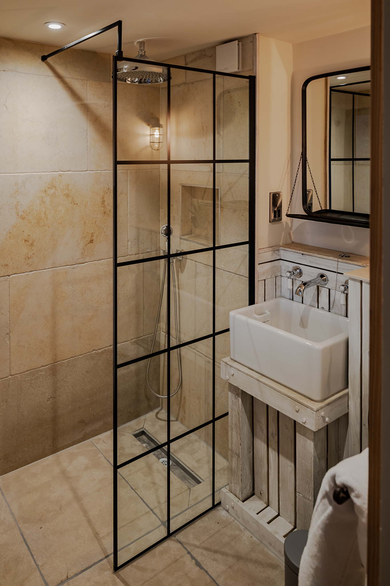 Modern bathroom with a glass shower partition, rainfall showerhead, rectangular sink, large mirror, and beige tiled walls. - Wild Thyme & Honey Hotel in the Cotswolds