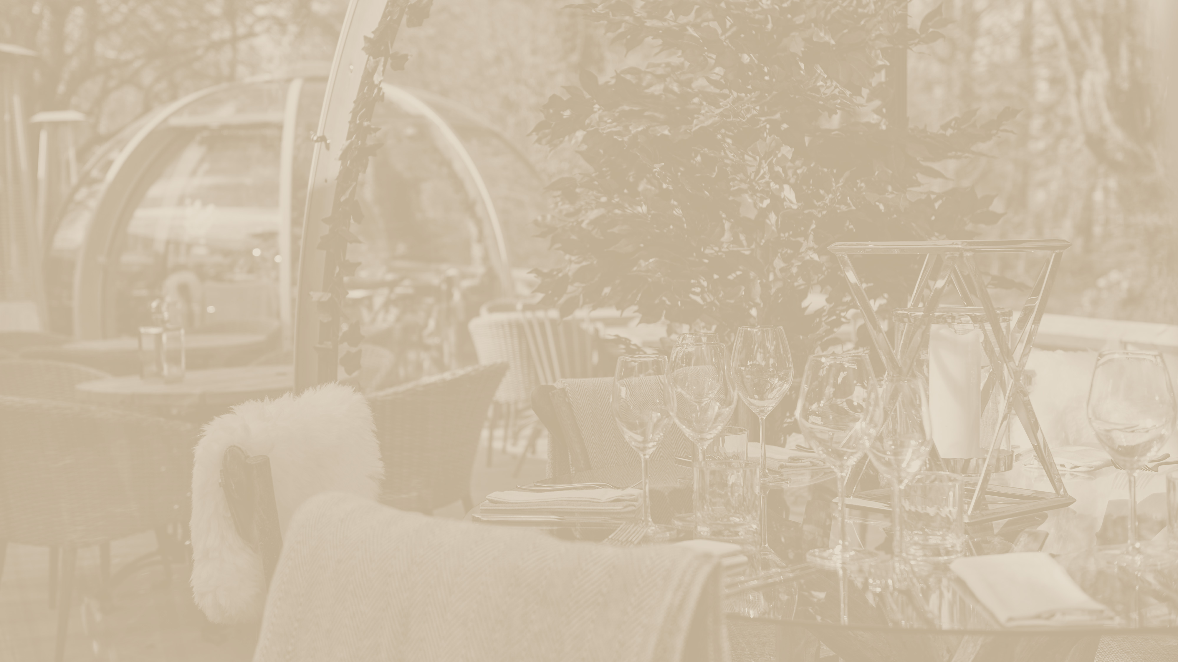 Outdoor dining area with tables set with glassware and napkins, surrounded by trees and a dome structure in the background. - Wild Thyme & Honey Hotel in the Cotswolds