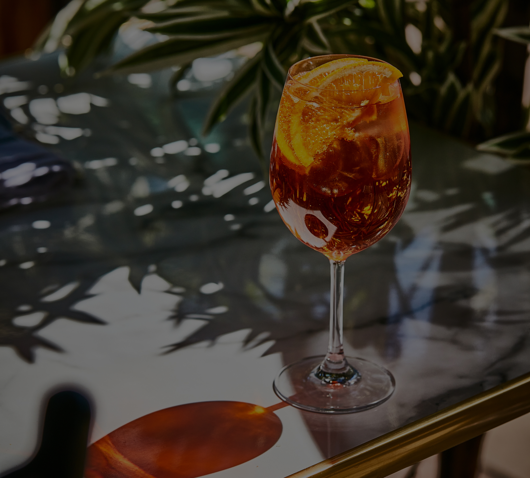 A glass of iced tea with lemon slices on a reflective table, surrounded by sunlight and shadow from nearby leaves. - Wild Thyme & Honey Hotel in the Cotswolds