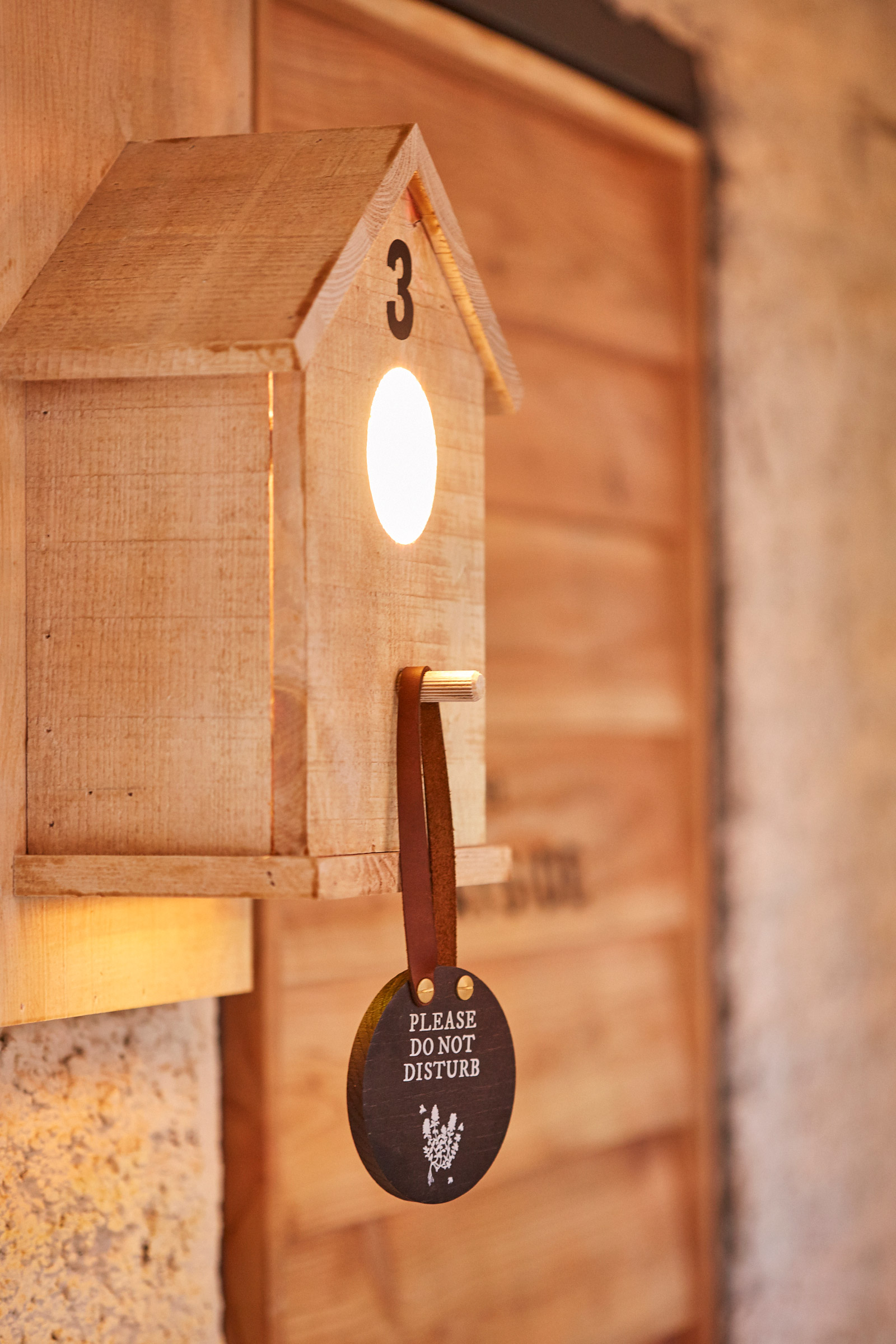 Wooden birdhouse with number 3, lit inside; a Please Do Not Disturb sign hangs from it, background is a wooden wall. - Wild Thyme & Honey Hotel in the Cotswolds