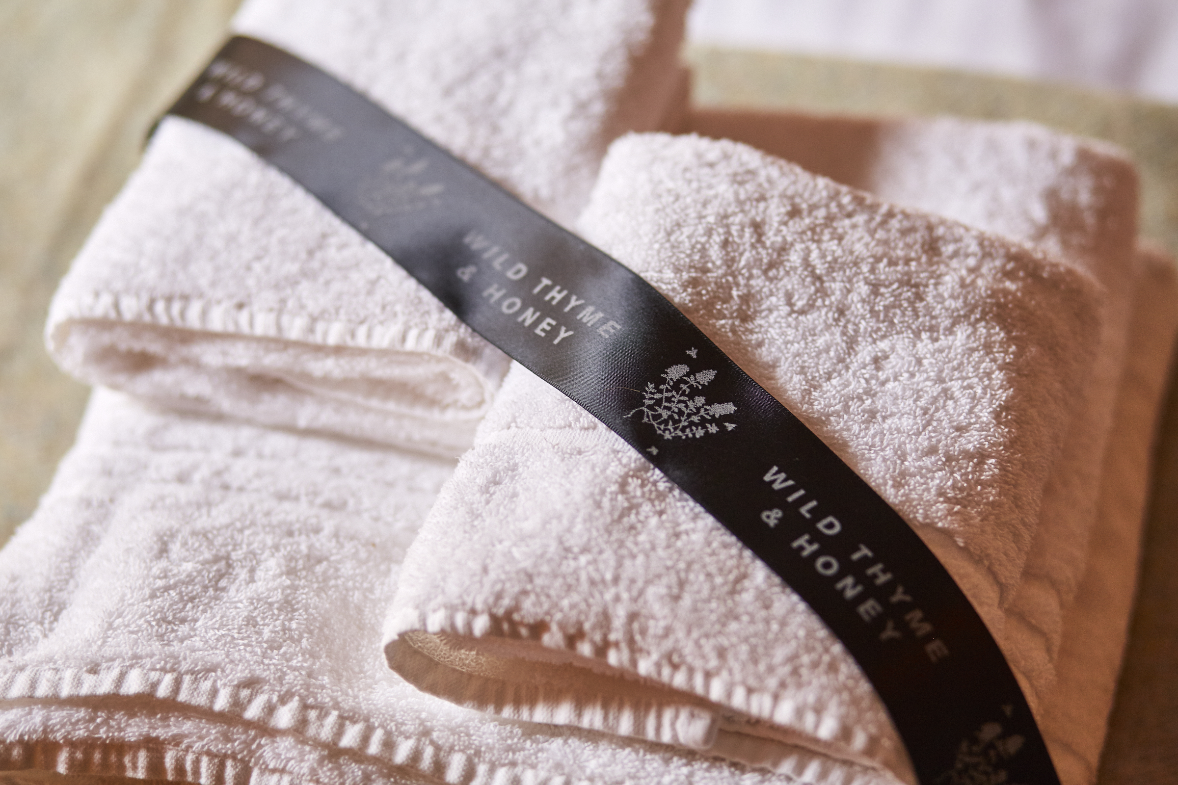 Two white towels neatly folded with a black ribbon labeled Wild Thyme & Honey placed on top. - Wild Thyme & Honey Hotel in the Cotswolds