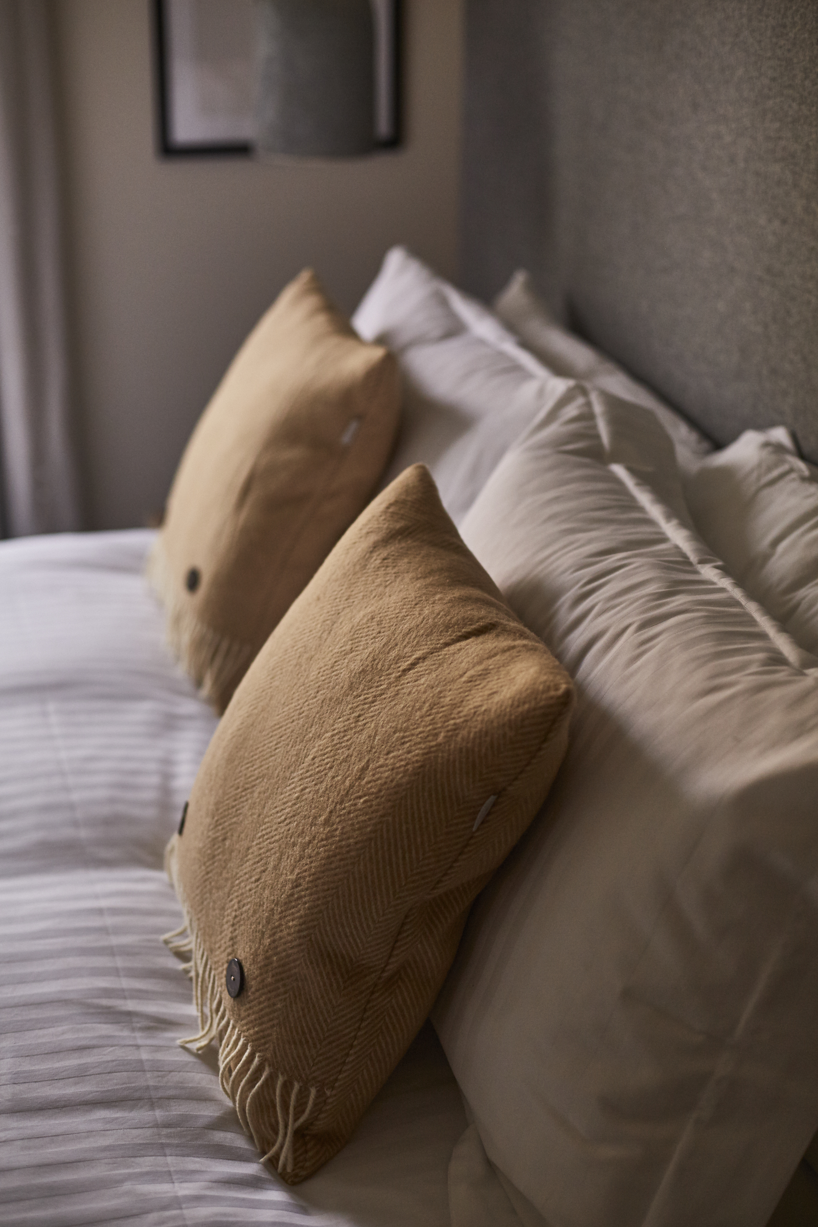 Close-up of a neatly made bed with white sheets and two large beige pillows, set against a textured gray wall. - Wild Thyme & Honey Hotel in the Cotswolds
