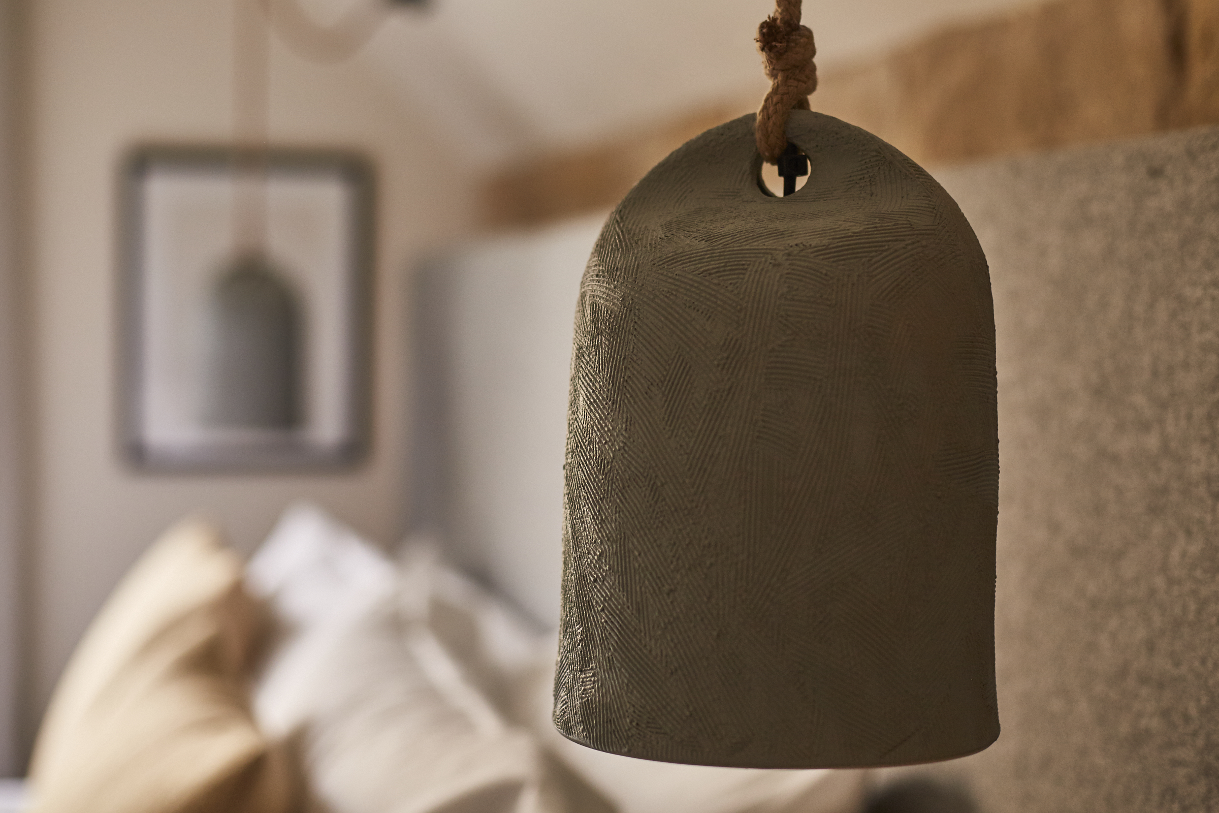 Close-up of a textured pendant light with a blurred background featuring pillows and part of a framed mirror. - Wild Thyme & Honey Hotel in the Cotswolds
