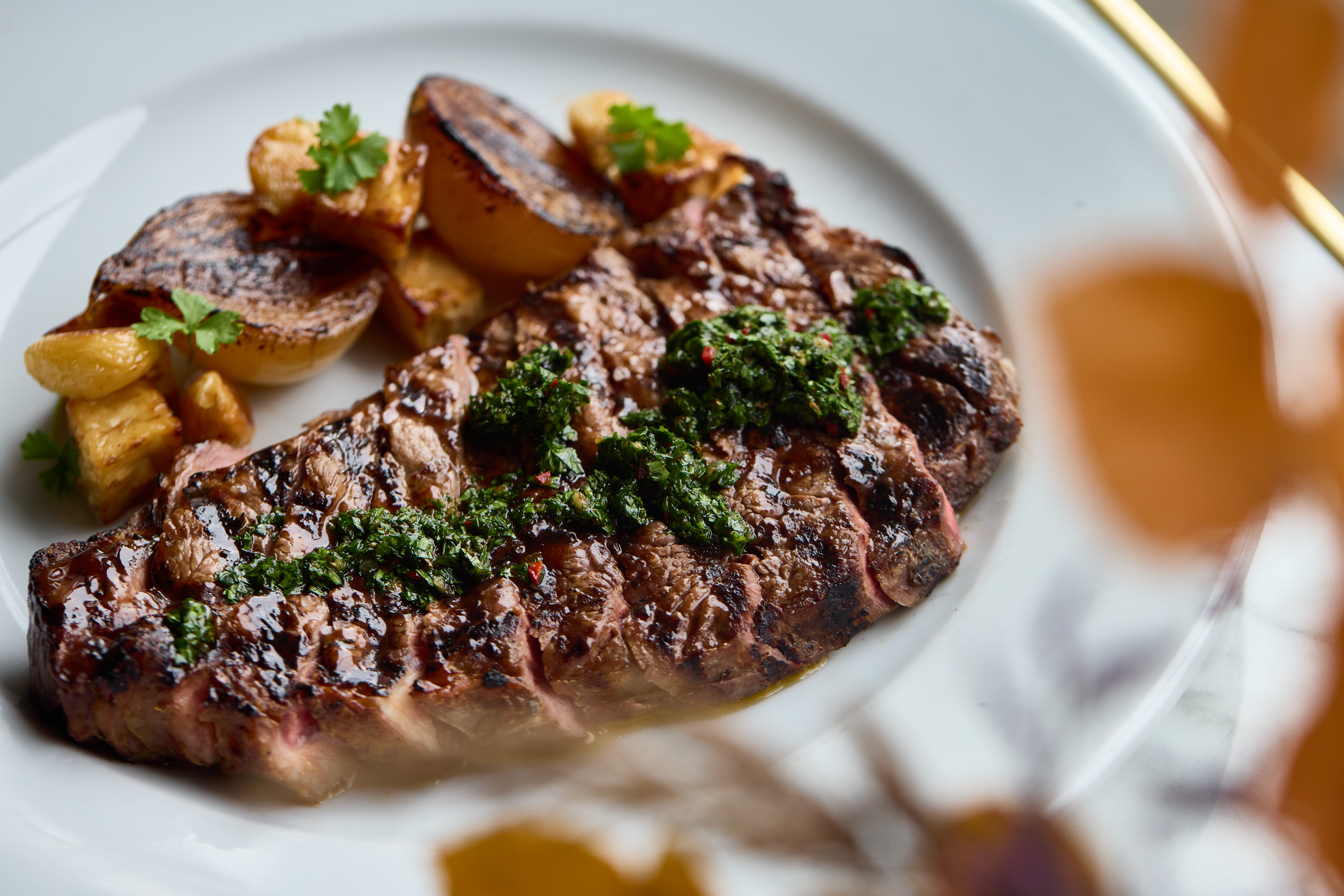 Grilled steak with green sauce on a plate, served with roasted potatoes and garnished with parsley. - Wild Thyme & Honey Hotel in the Cotswolds