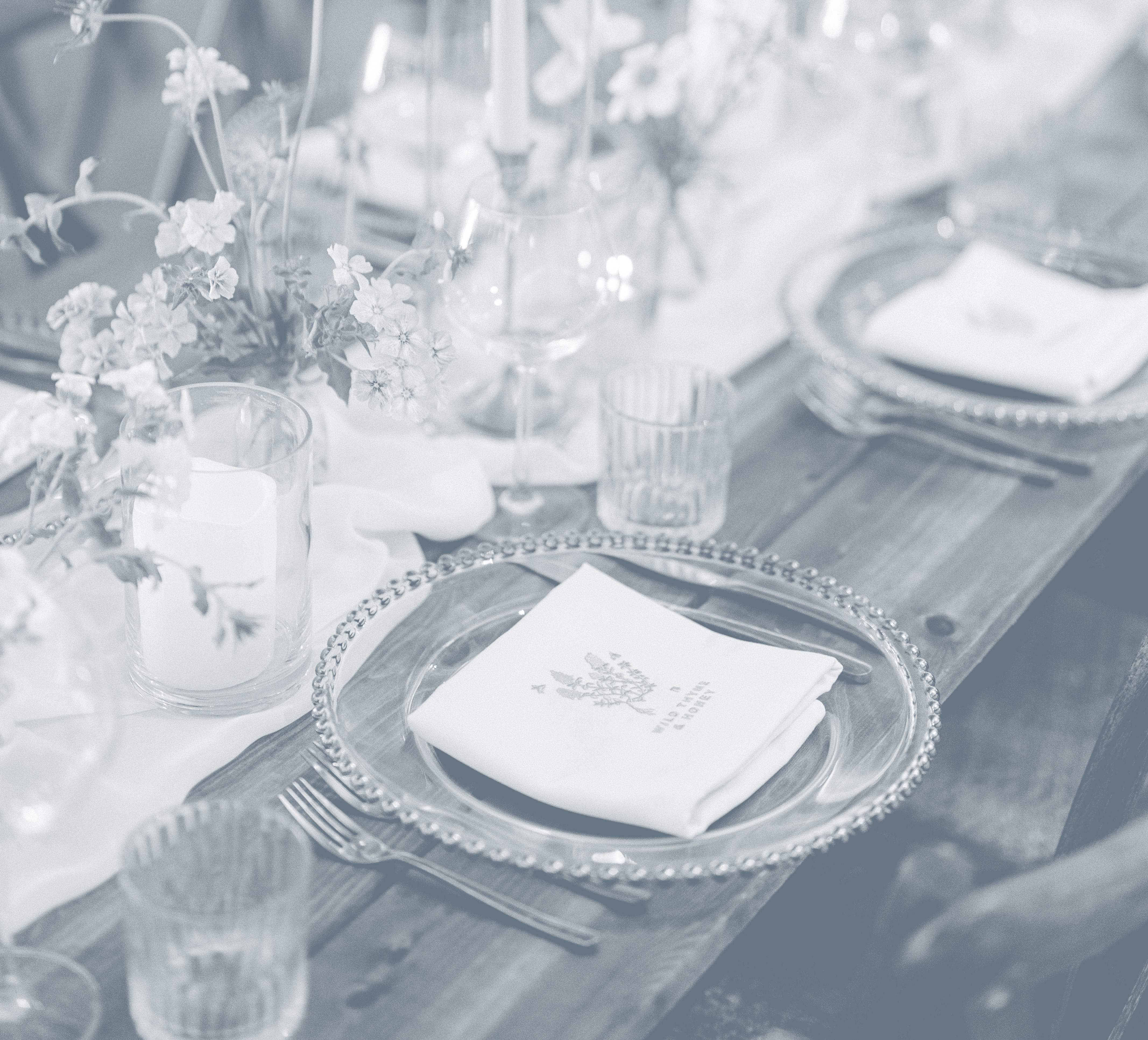 Elegant table setting with glass plates, folded napkins, candles, and flowers on a long wooden table. - Wild Thyme & Honey Hotel in the Cotswolds