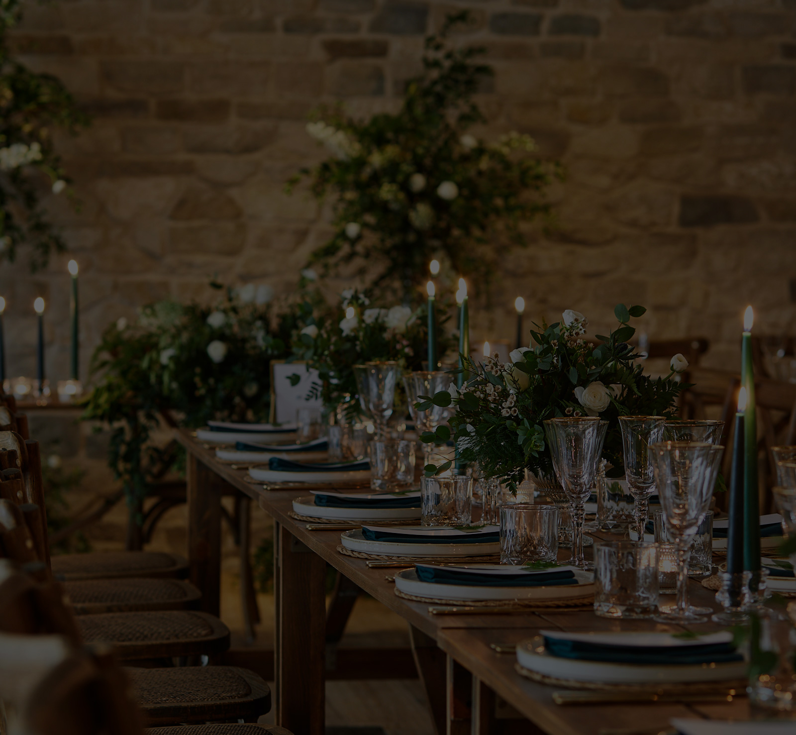 Candlelit dining table set for a formal event with elegant glassware, plates, and greenery against a stone wall background. - Wild Thyme & Honey Hotel in the Cotswolds