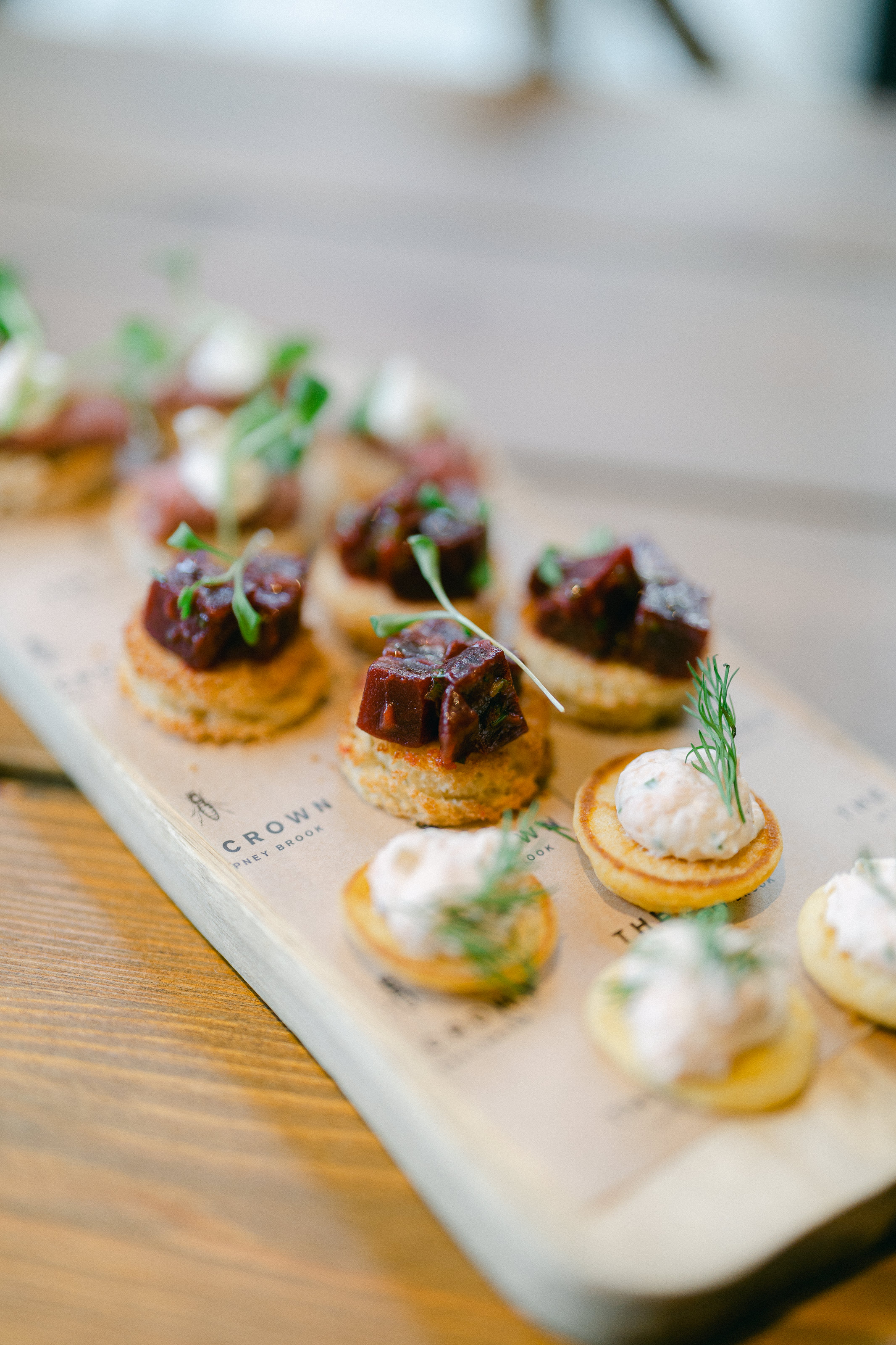 Assorted canapés on a wooden tray, topped with meat, dill cream, and garnishes. - Wild Thyme & Honey Hotel in the Cotswolds