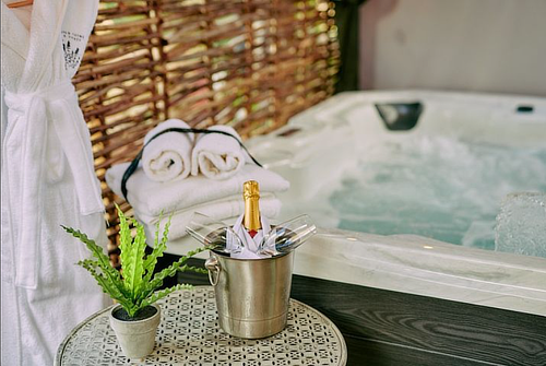 A jacuzzi with bubbling water, a towel rack with folded towels, a robe hanging, a champagne bottle in ice, and a potted plant. - Wild Thyme & Honey Hotel in the Cotswolds