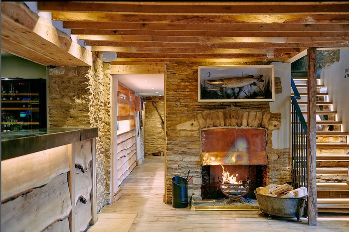 Rustic living room with stone walls, wooden beams, and a lit fireplace. A staircase is on the right. Cozy and inviting ambiance. - Wild Thyme & Honey Hotel in the Cotswolds
