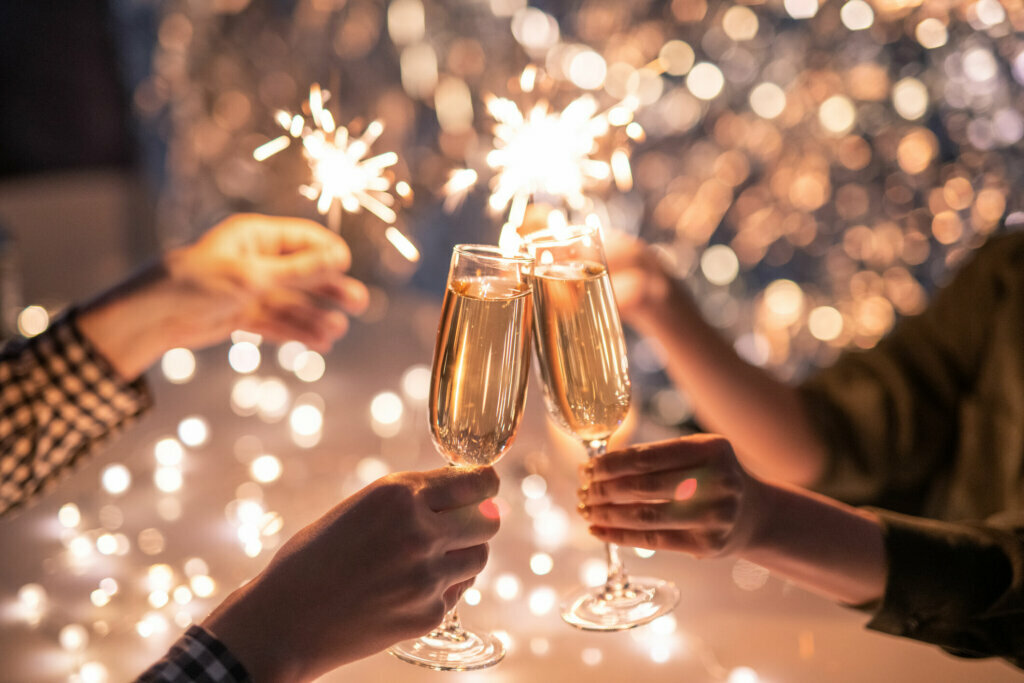 Hands holding champagne glasses and sparklers with a bokeh background, celebrating in a festive setting. - Wild Thyme & Honey Hotel in the Cotswolds