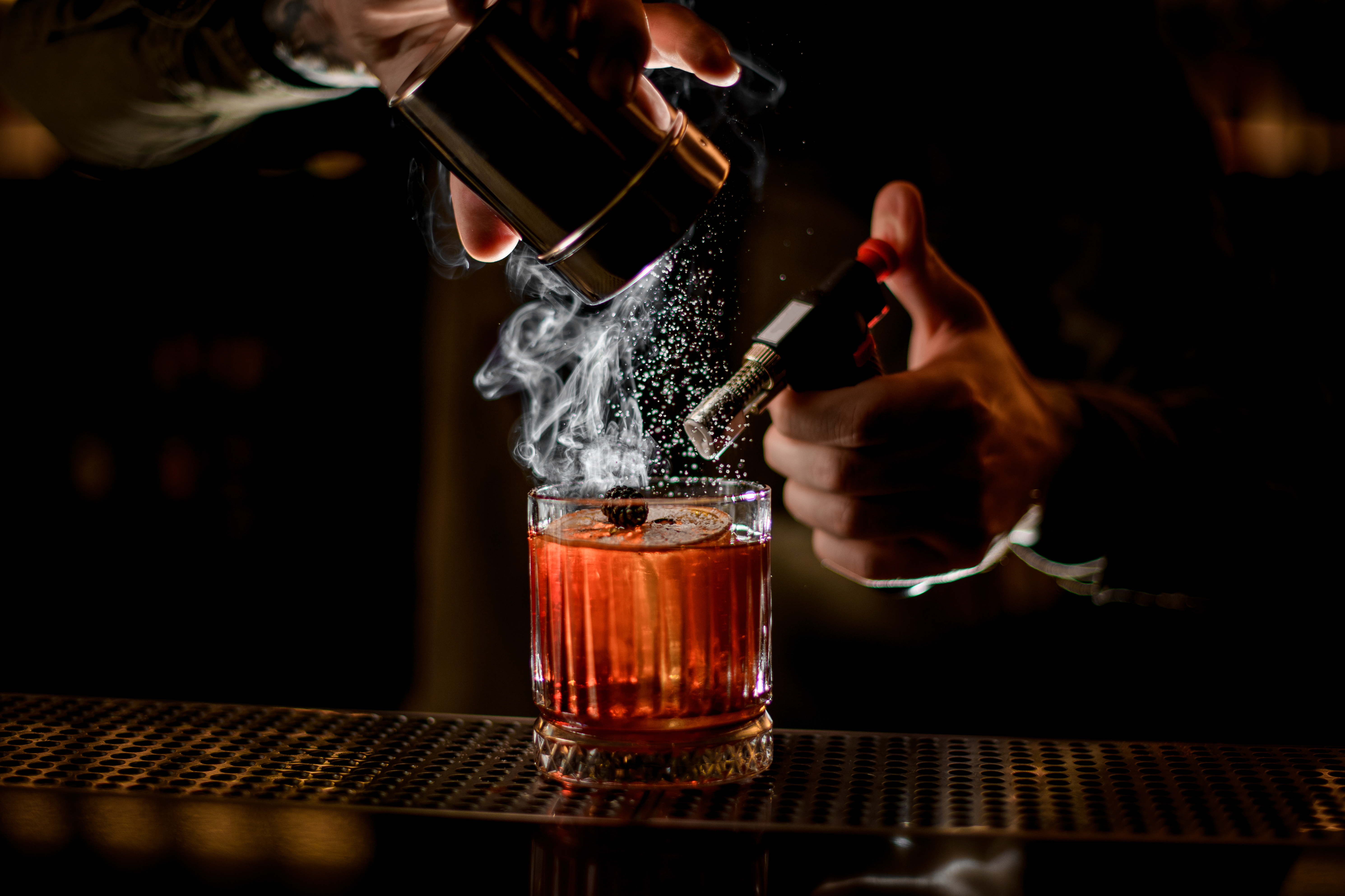 A cocktail being prepared with a torch and shaker, emitting smoke, on a bar counter. - Wild Thyme & Honey Hotel in the Cotswolds