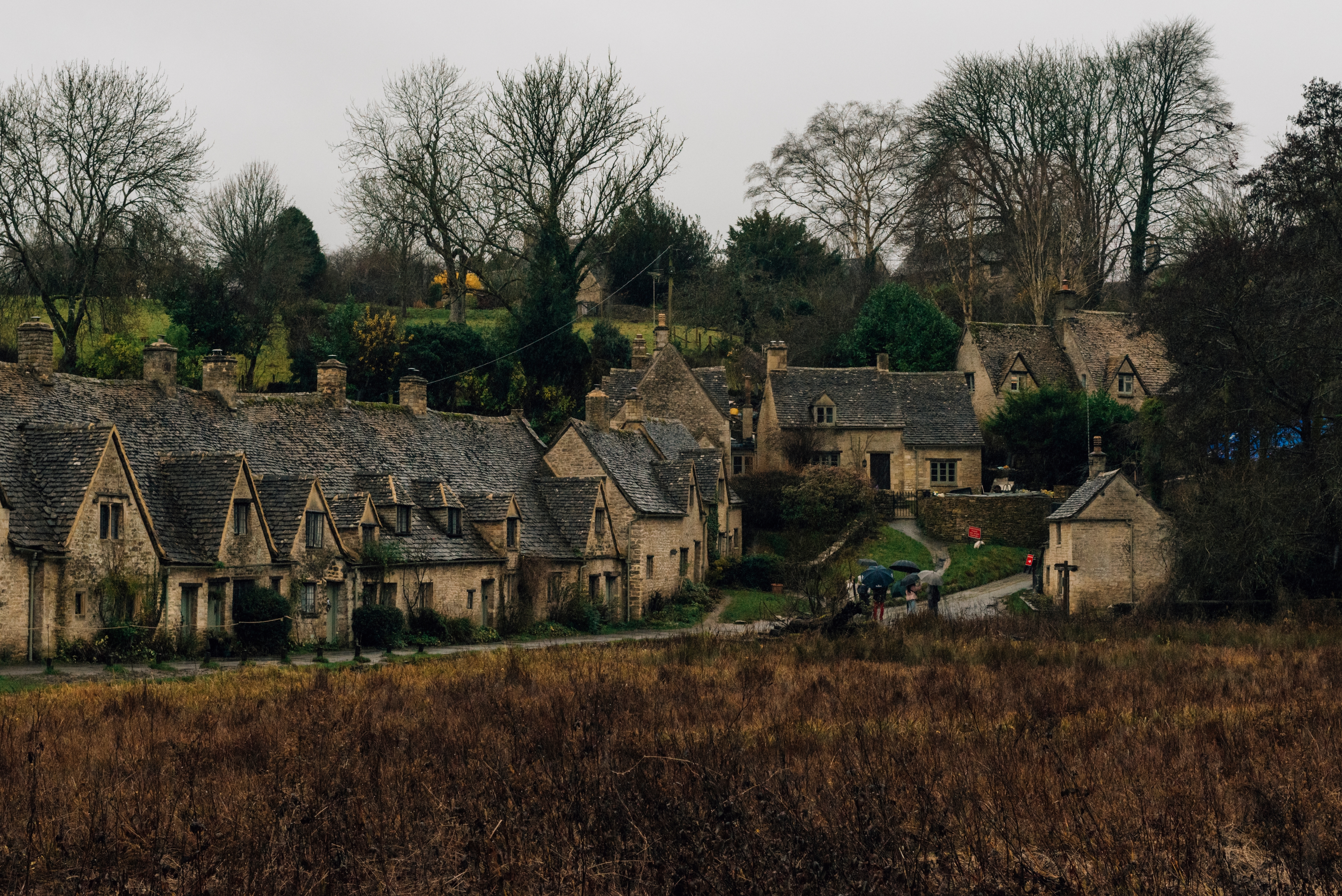 Quaint stone cottages with thatched roofs in a rural village, surrounded by bare trees on an overcast day. - Wild Thyme & Honey Hotel in the Cotswolds