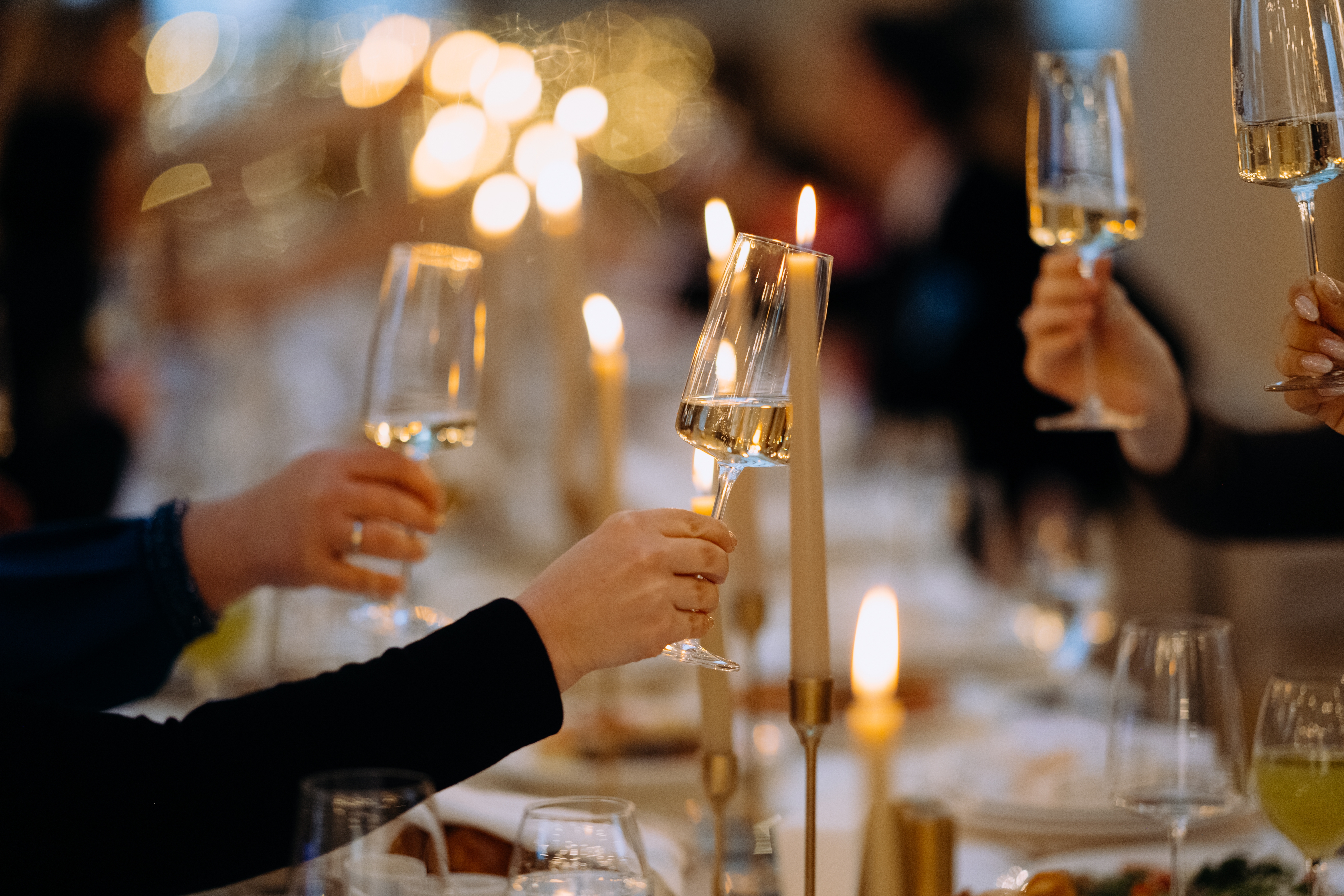 People raise champagne glasses in a toast over a candlelit table set for a formal dinner. - Wild Thyme & Honey Hotel in the Cotswolds