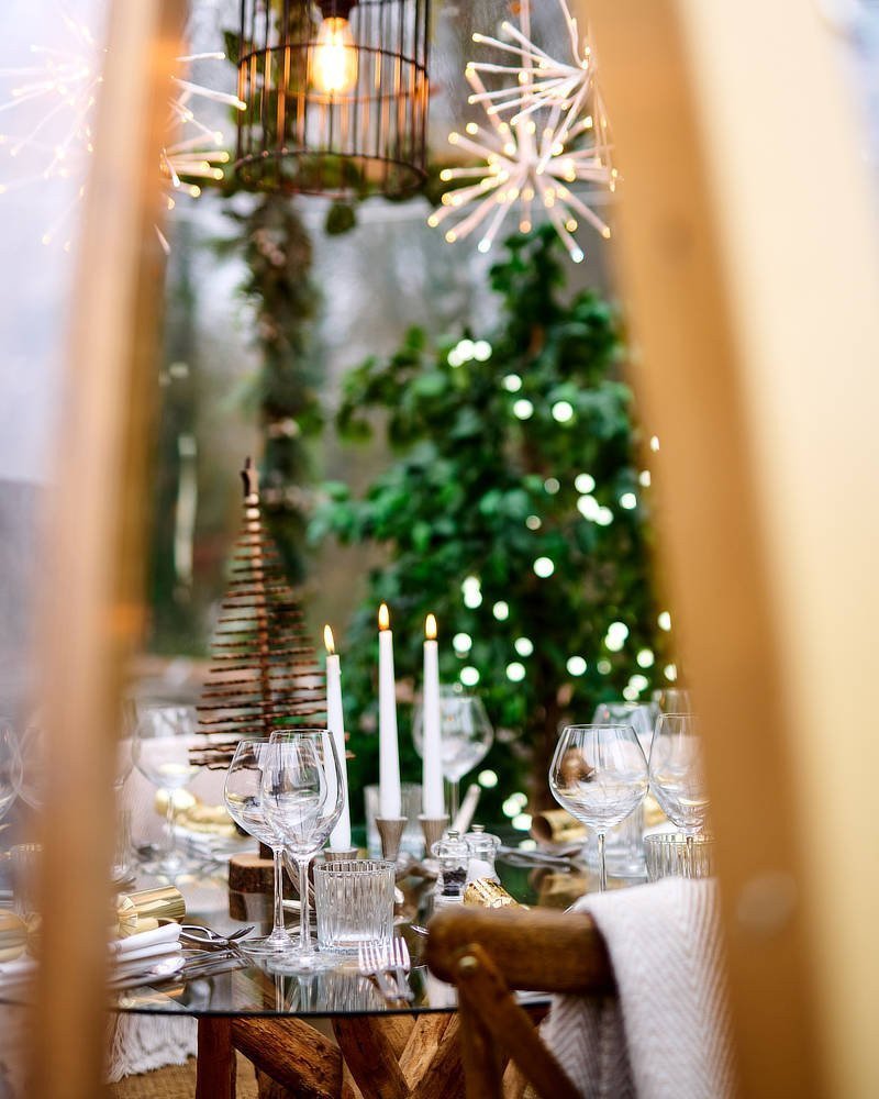 Elegant holiday table setting with candles, wine glasses, and festive decorations, surrounded by greenery and twinkling lights. - Wild Thyme & Honey Hotel in the Cotswolds
